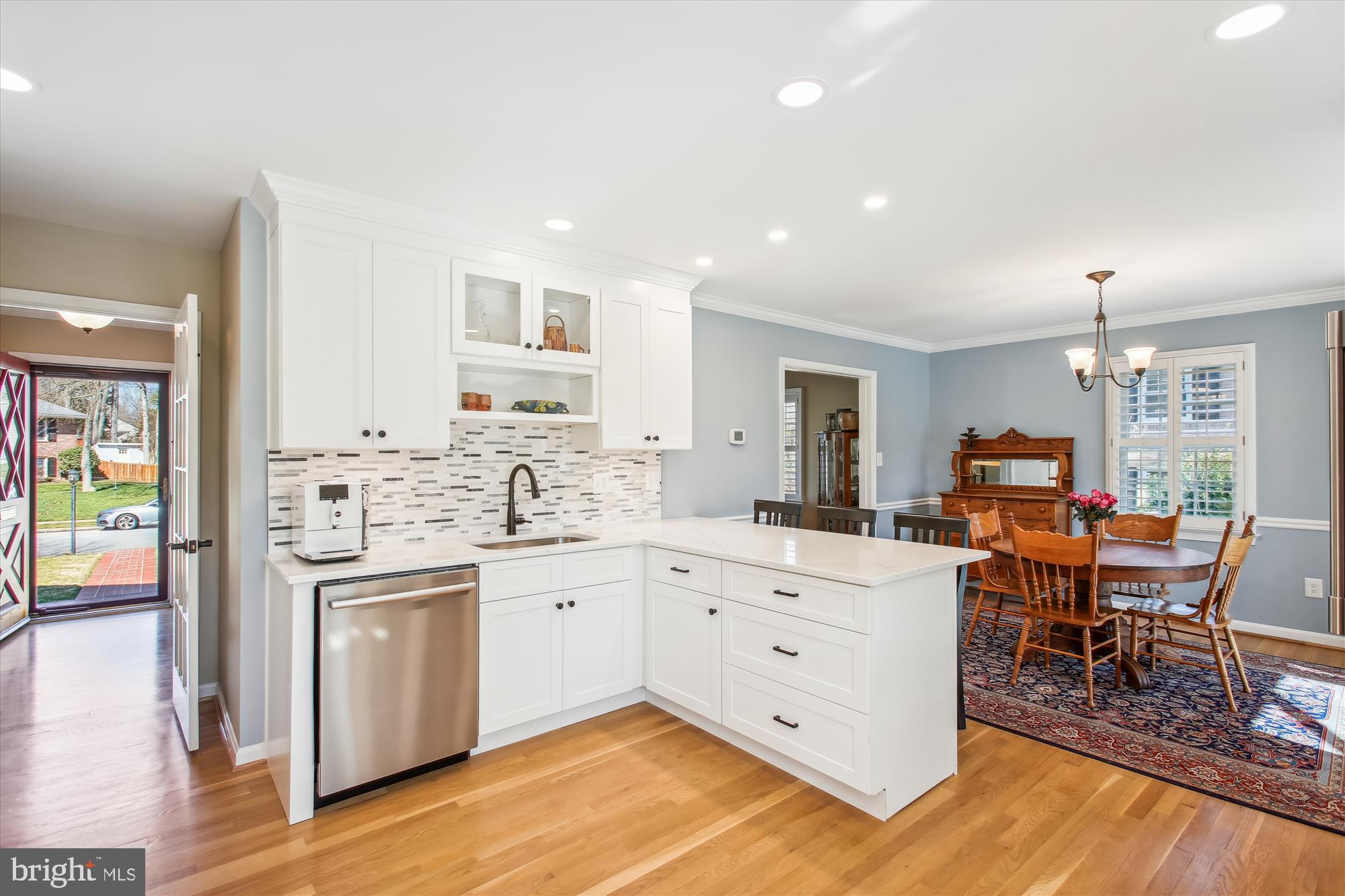 Kitchen with a white island and tile backsplash, opening into a dining room with wooden furniture.