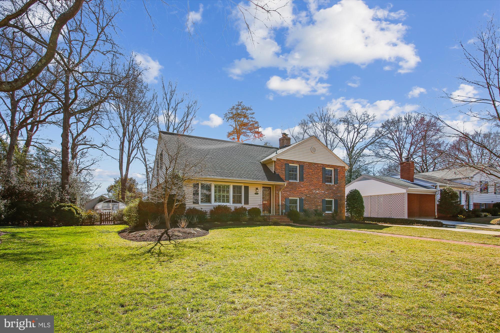 Two-story brick-and-siding home with dark shutters and a broad lawn, framed by mature trees.