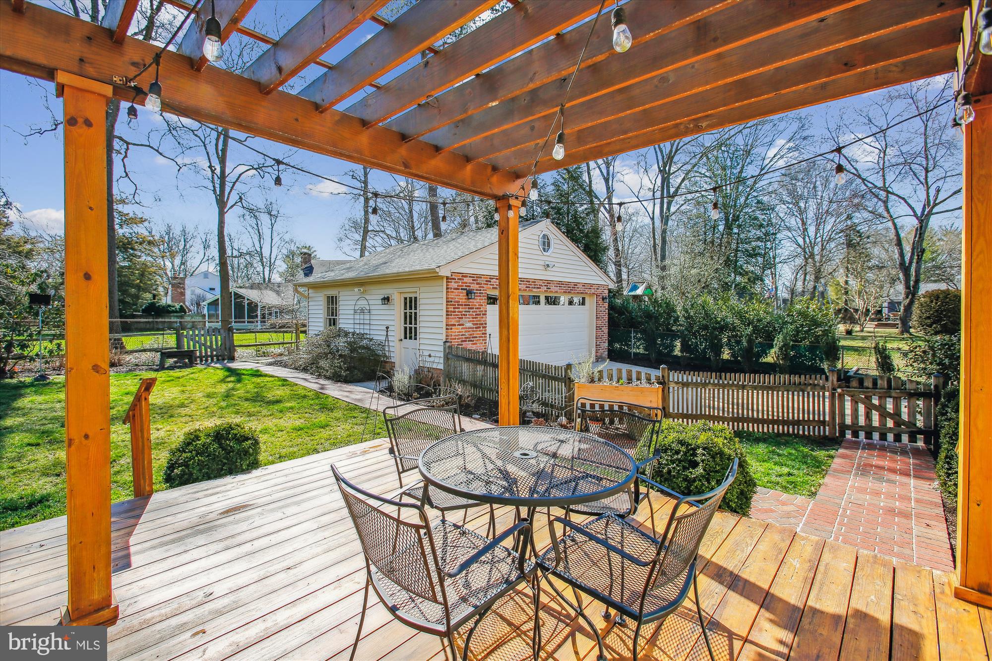 Pergola-covered deck with patio dining set, overlooking a fenced yard and detached garage.