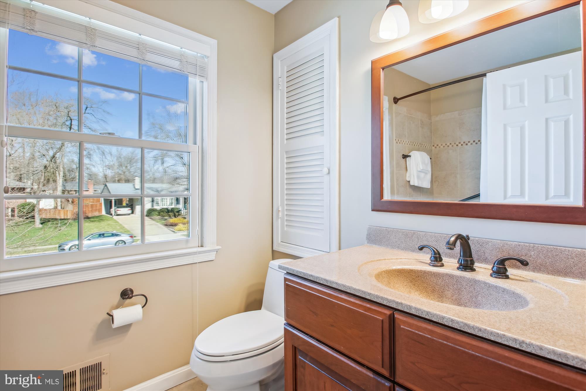 Bathroom with a wood vanity and large window; the mirror reflects a tiled shower.
