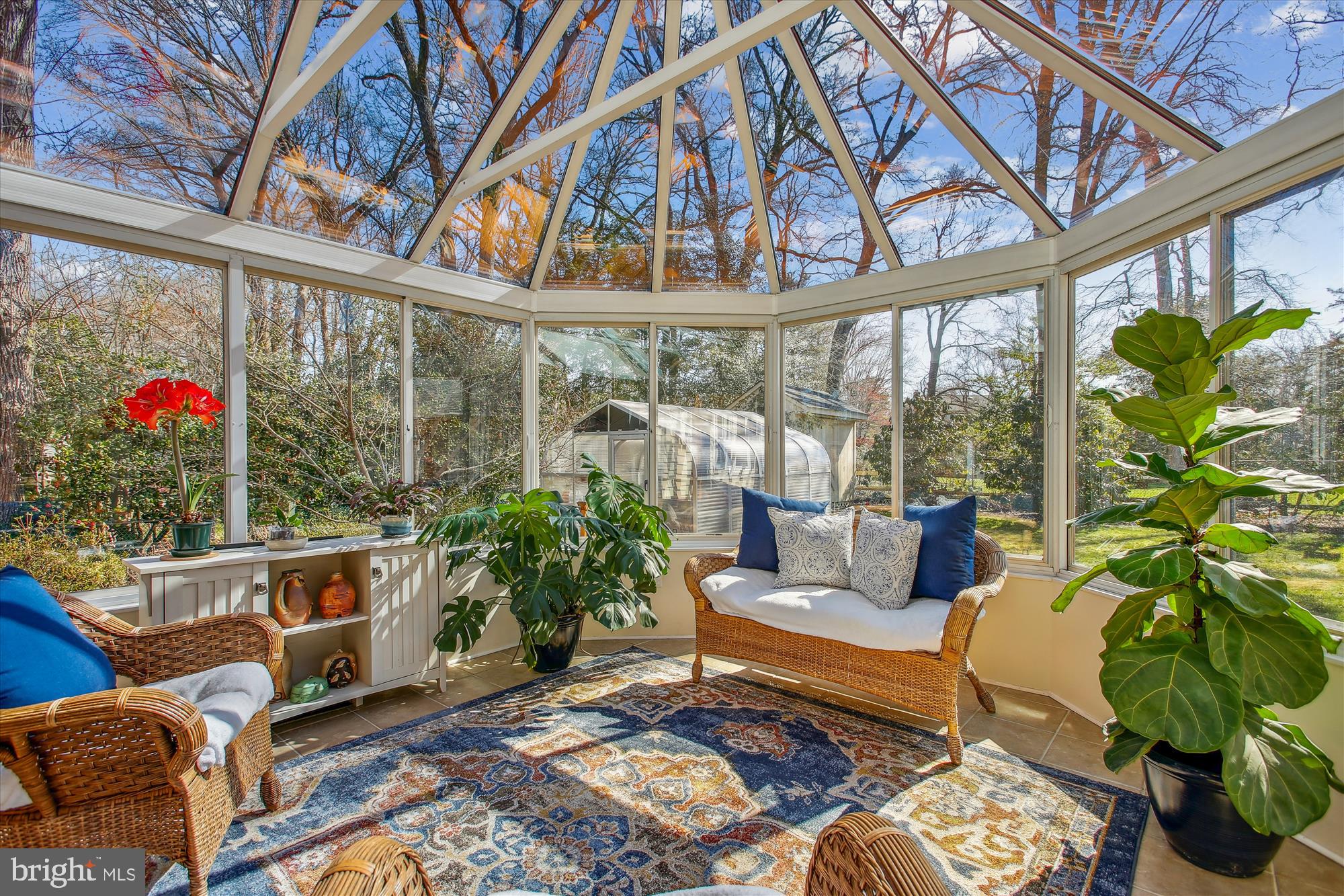 Furnished sunroom with a vaulted glass ceiling, wicker seating, and leafy plants.