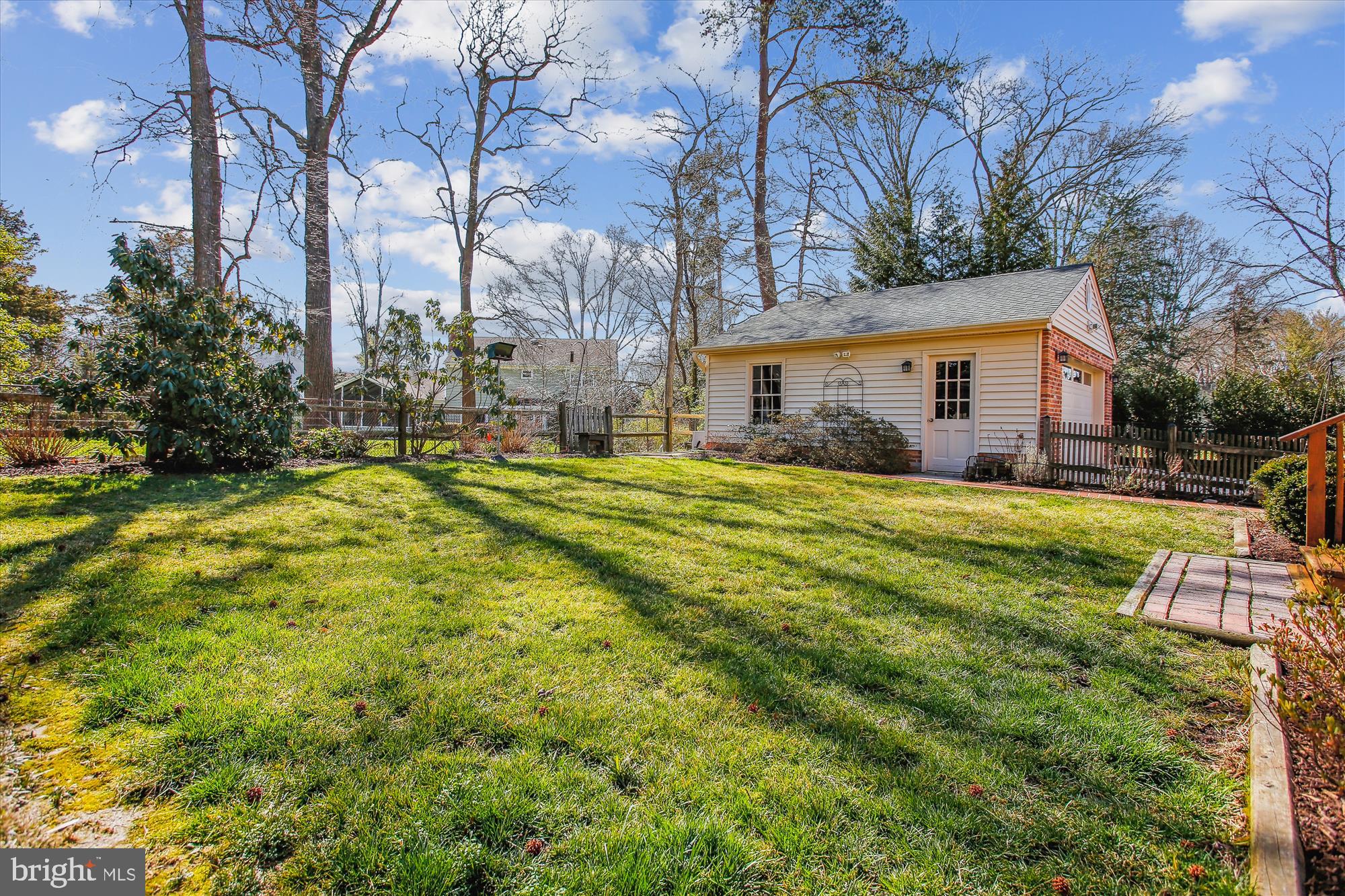 Grassy backyard with a detached white outbuilding, wooden fence, and mature trees.