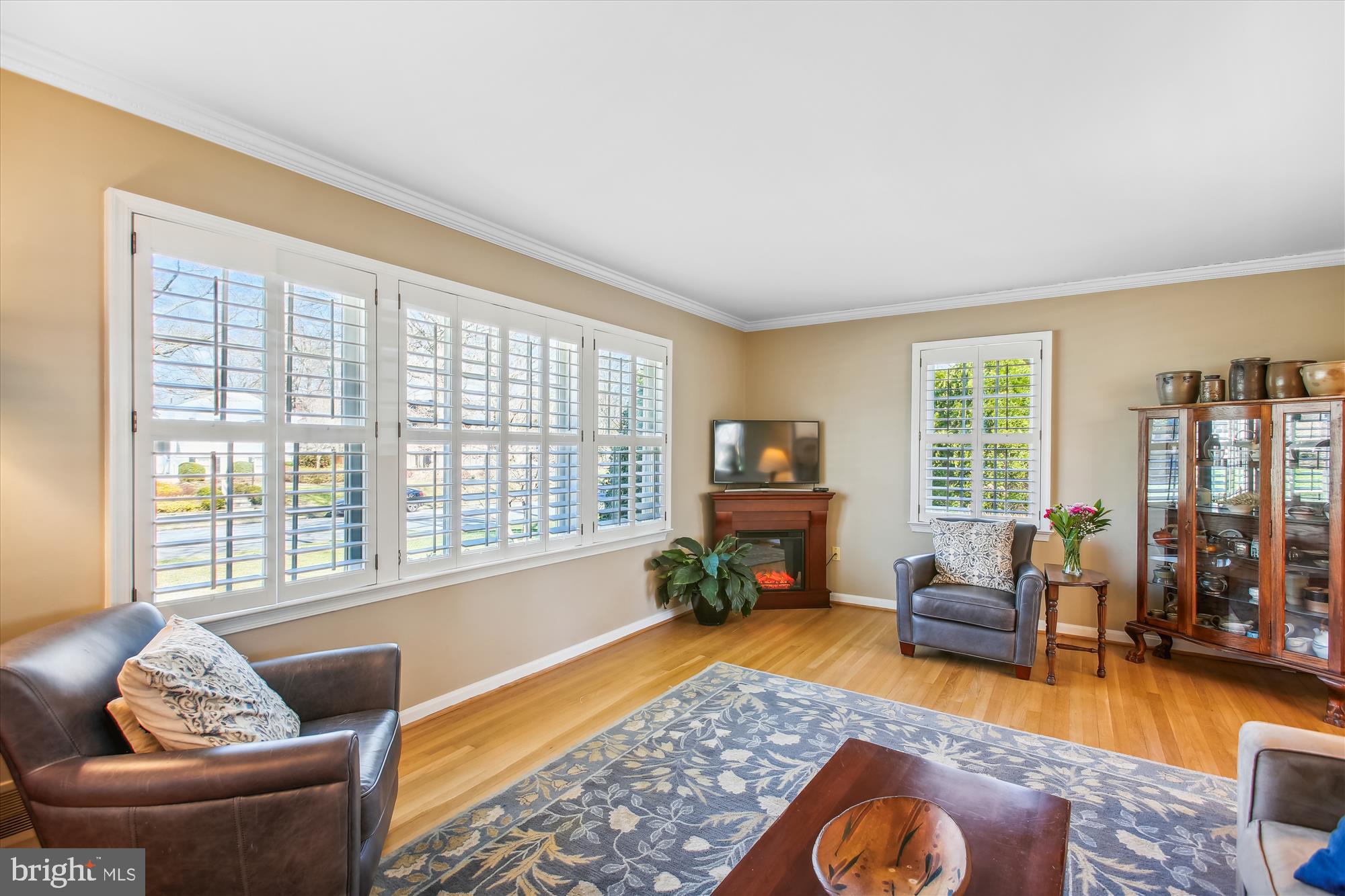 Living room with plantation shutters, hardwood floors, leather seating, and a corner fireplace.