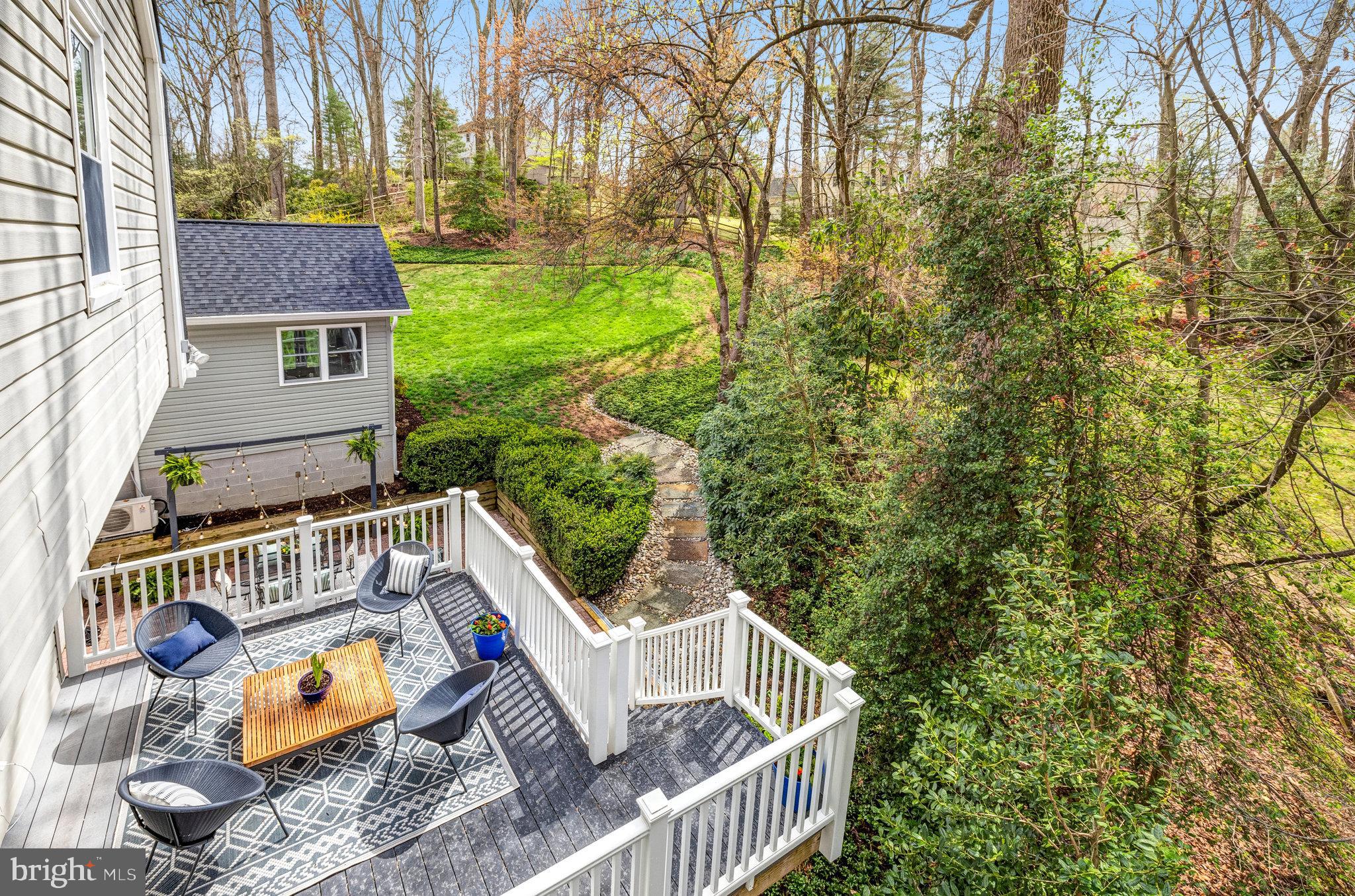 Furnished deck with white railings overlooks a green lawn and wooded backyard.