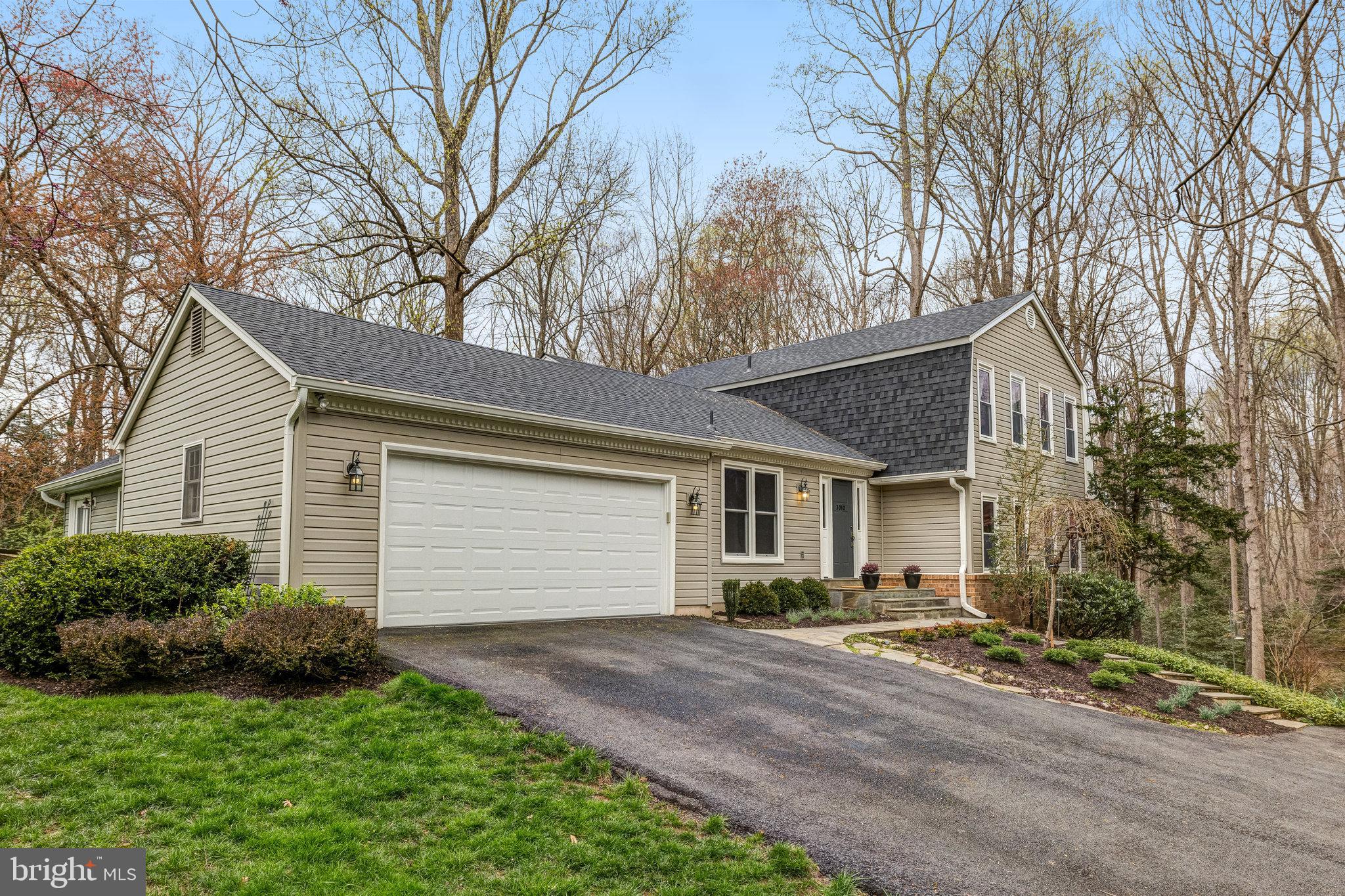 Beige-sided house with a double garage and paved driveway, surrounded by leafless trees.