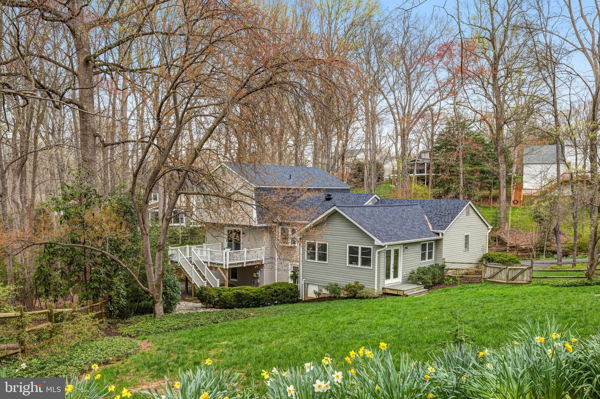 Gray-sided home with raised deck, wooded surroundings, and daffodils along the lawn.