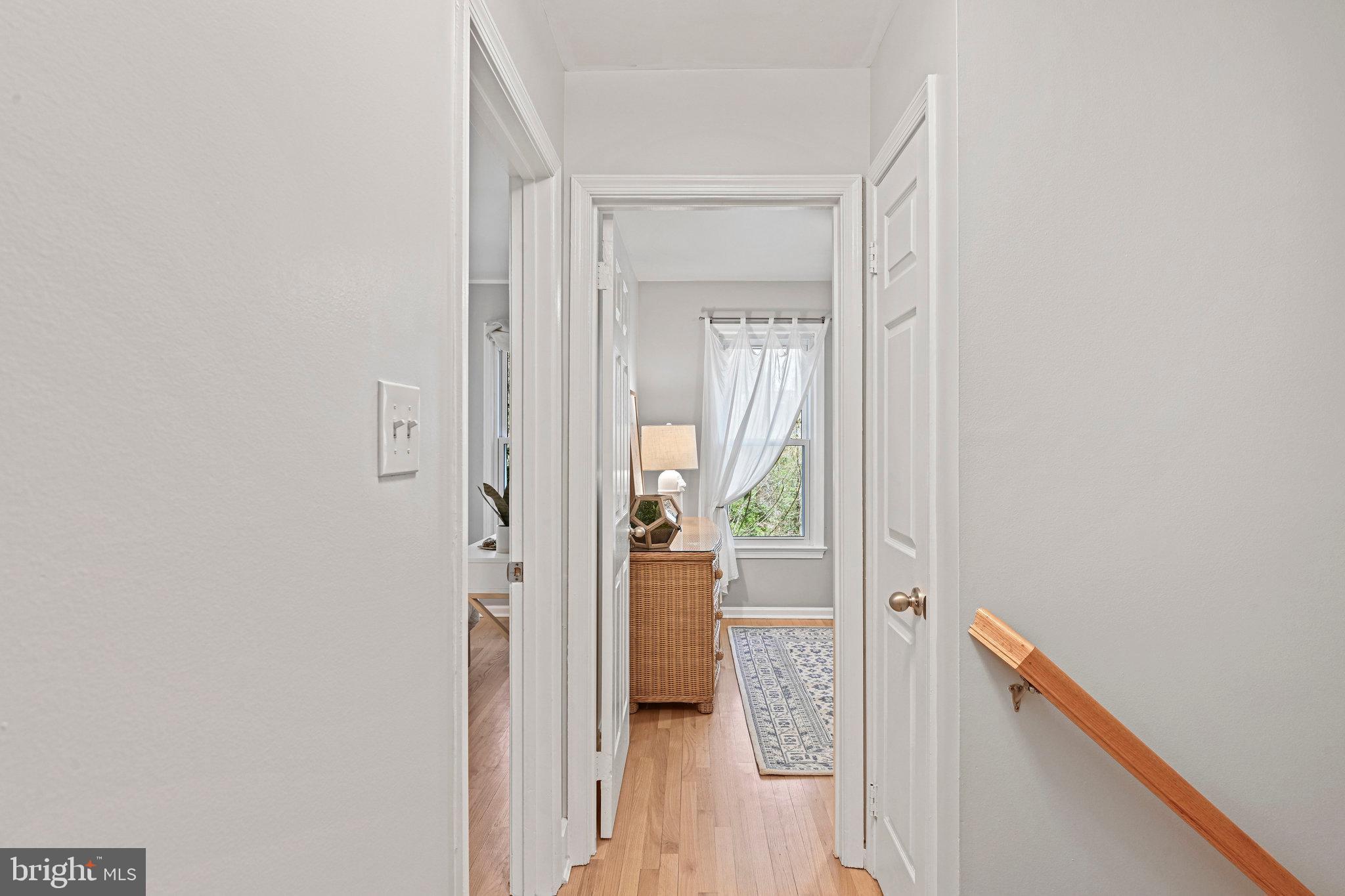 Hallway opening to a bedroom with a wicker dresser, patterned rug, and window with sheer curtains.
