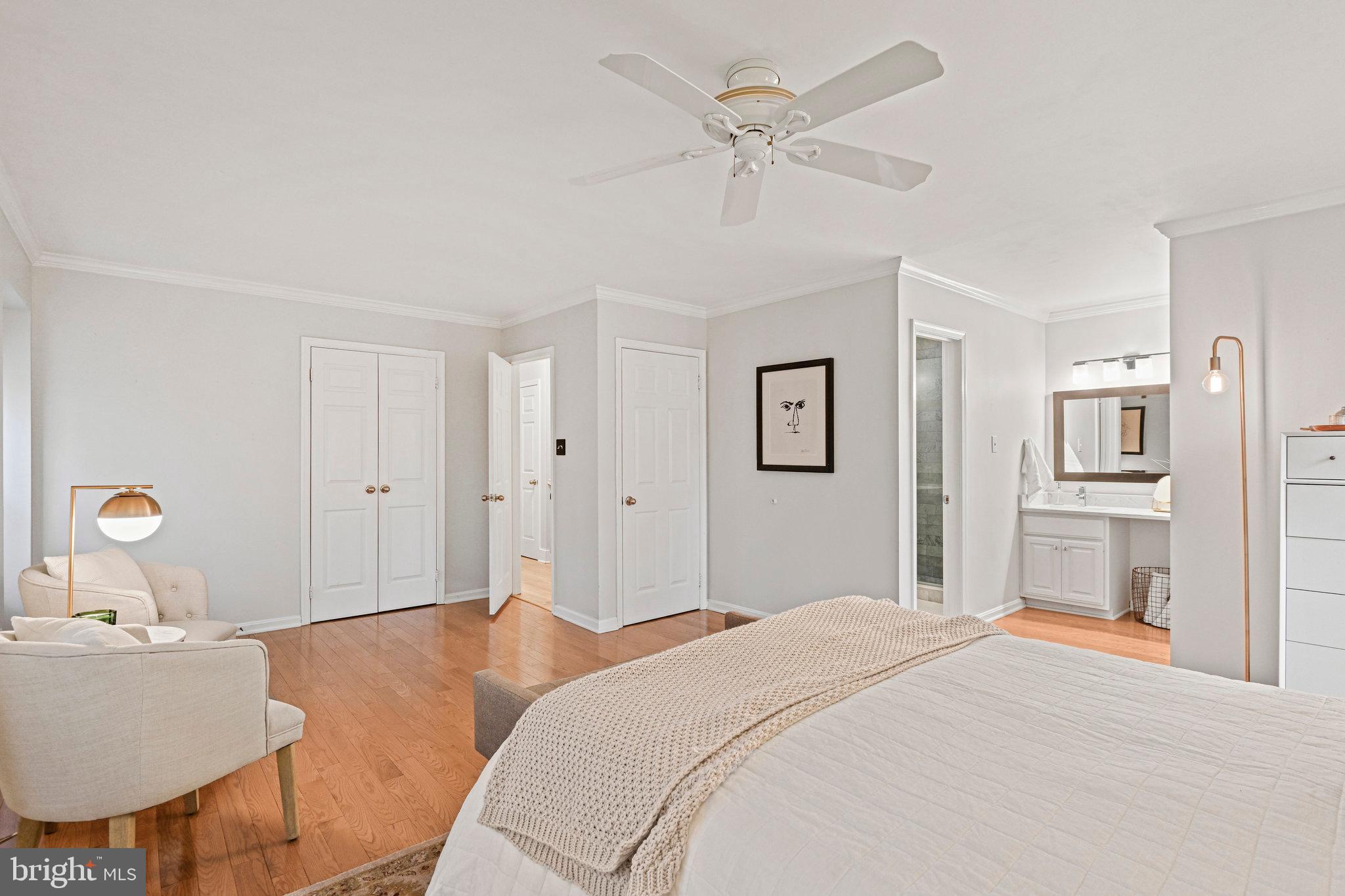 Bedroom with a large bed, sitting area, hardwood floors, ceiling fan, and adjoining bathroom.
