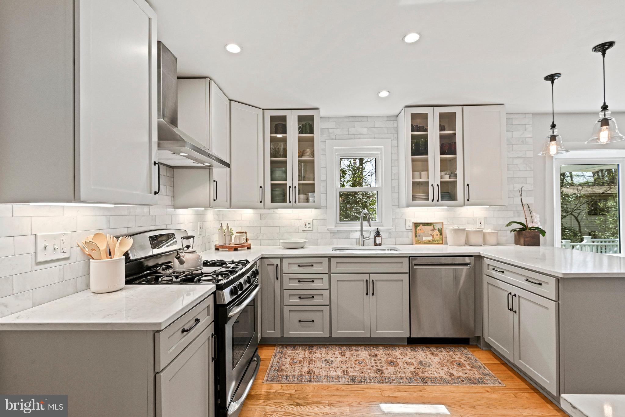Bright kitchen with white and gray cabinets, subway tile backsplash, stainless appliances, and hardwood floors.