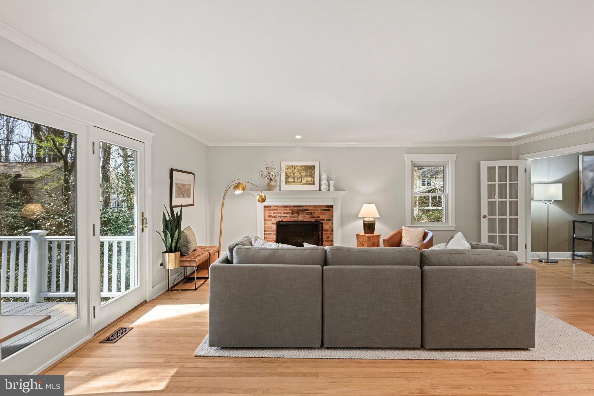 Living room with a gray sectional, brick fireplace, hardwood floors, and French doors opening to a deck.