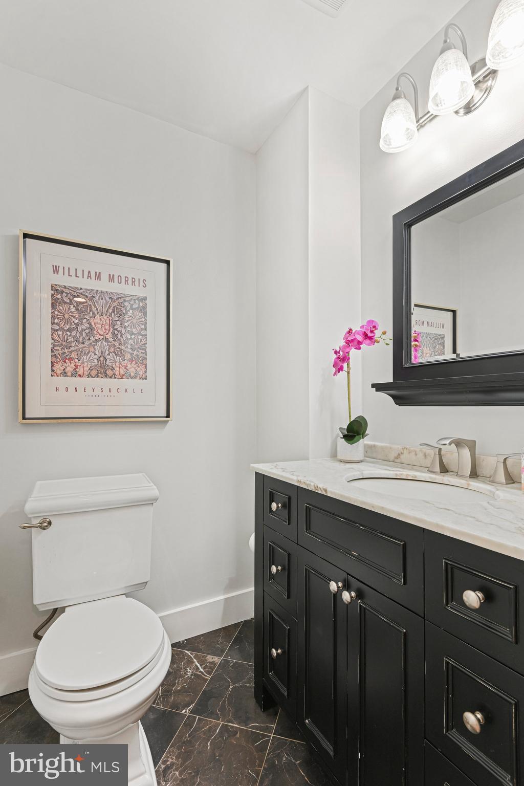 Powder room with black vanity, marble counter, white toilet, and framed floral print.