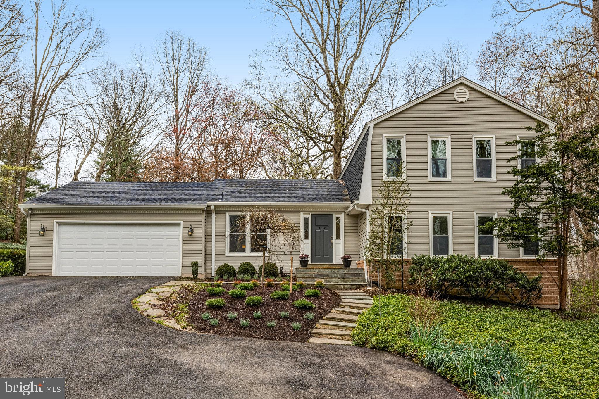 Beige-sided home with an attached garage, landscaped garden beds, and a stone walkway to the front door.