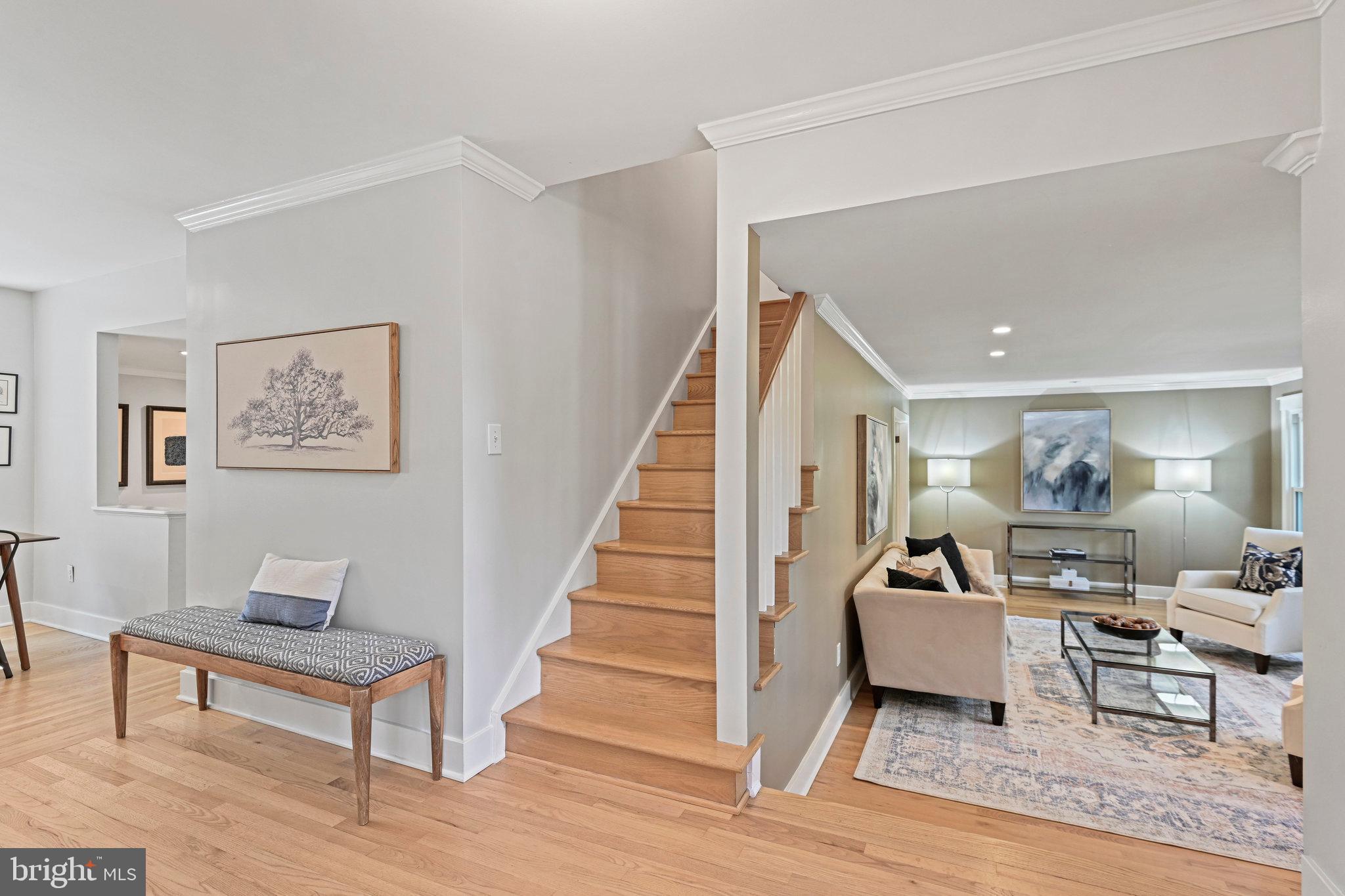 Entryway with hardwood floors and staircase opening to a staged living room.