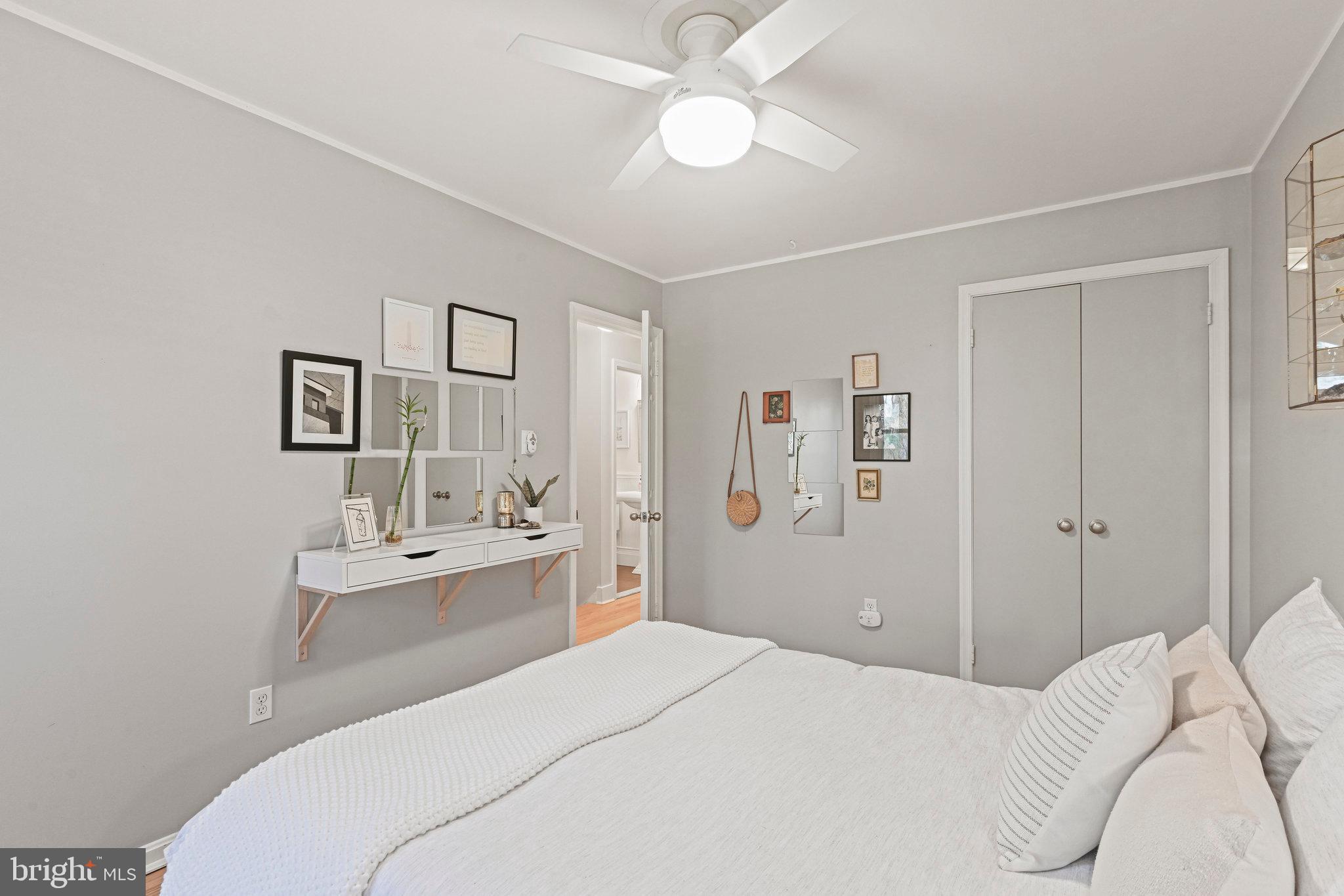 Bedroom with a white bed, gray walls, ceiling fan, and framed art above a console table.
