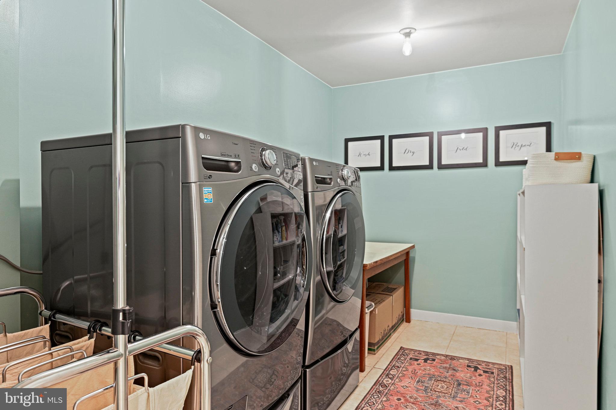 Laundry room with gray front-load washer and dryer, drying rack, and framed Wash, Dry, Fold, Repeat prints.