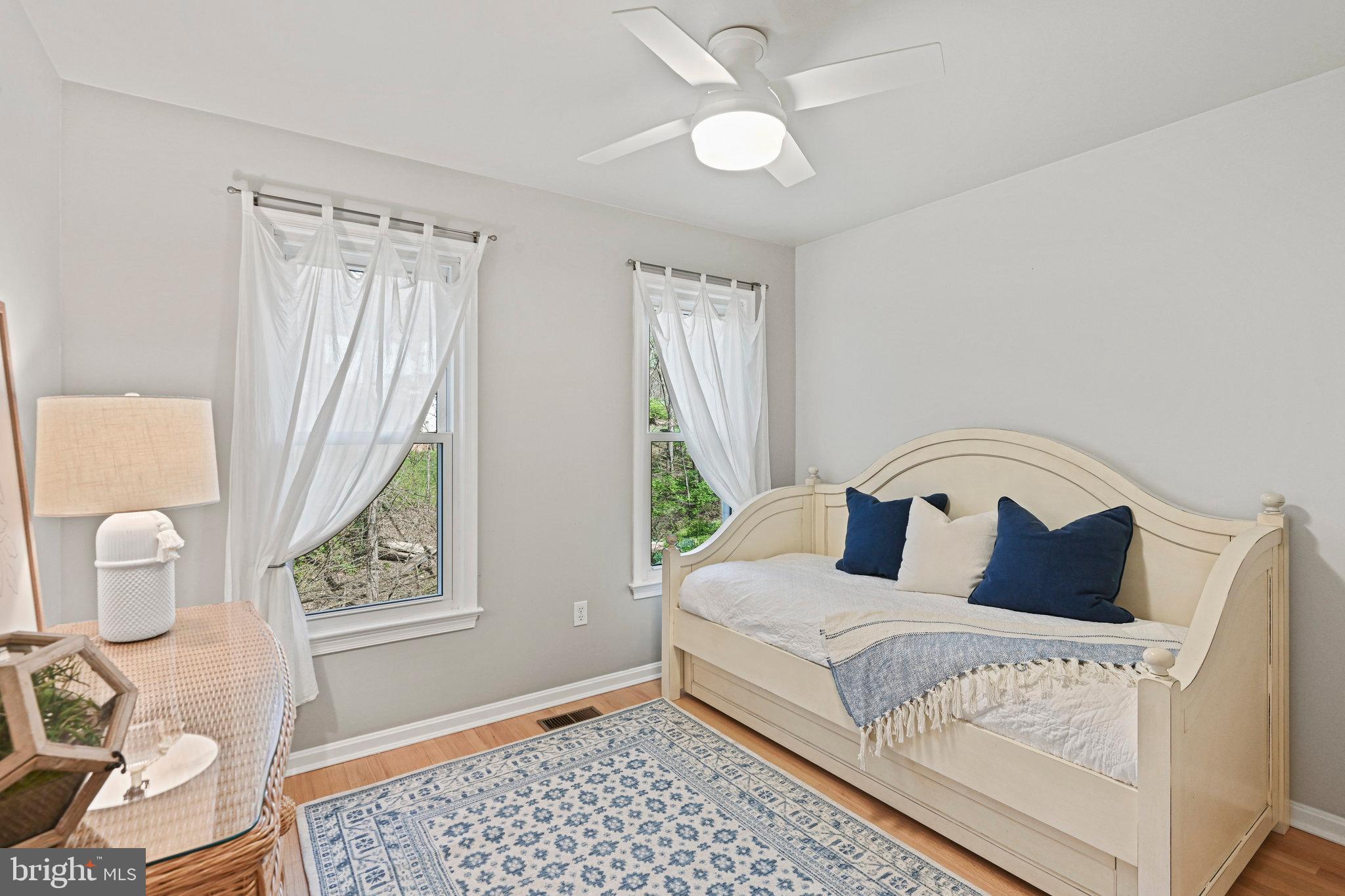Bedroom with a cream daybed, navy pillows, two curtained windows, and a blue patterned rug.