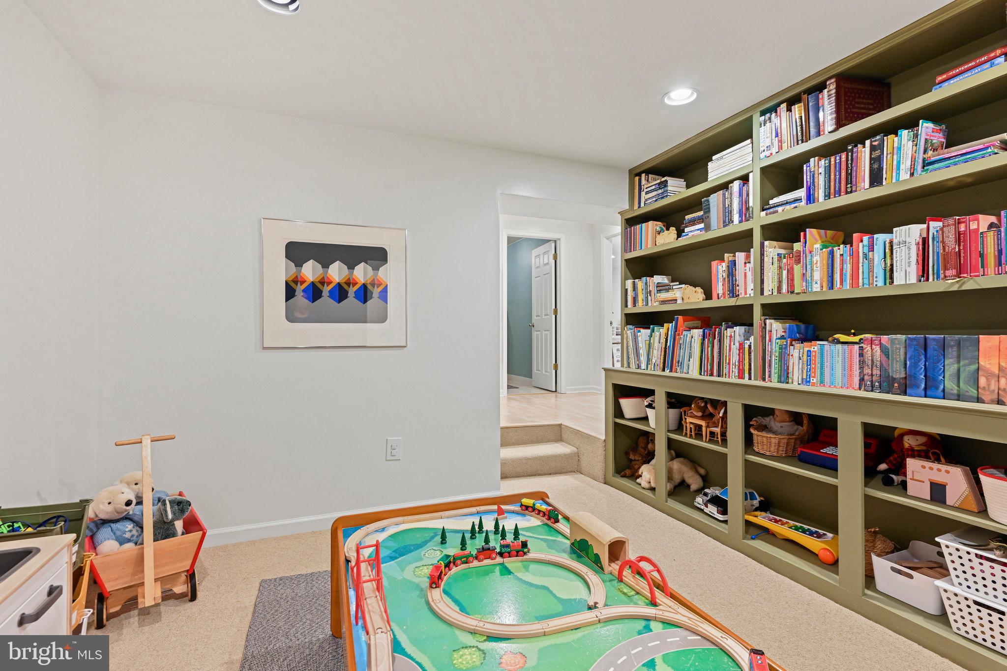 Playroom with built-in bookshelves, a wooden train table, toys and stuffed animals.