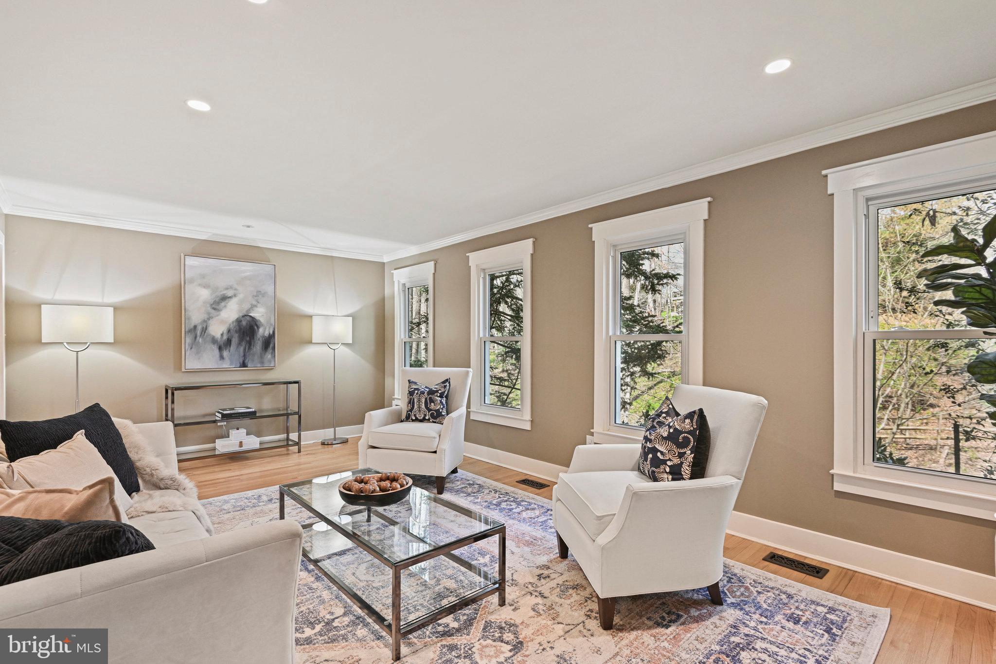 Staged living room with a cream sofa, white armchairs, and large windows.