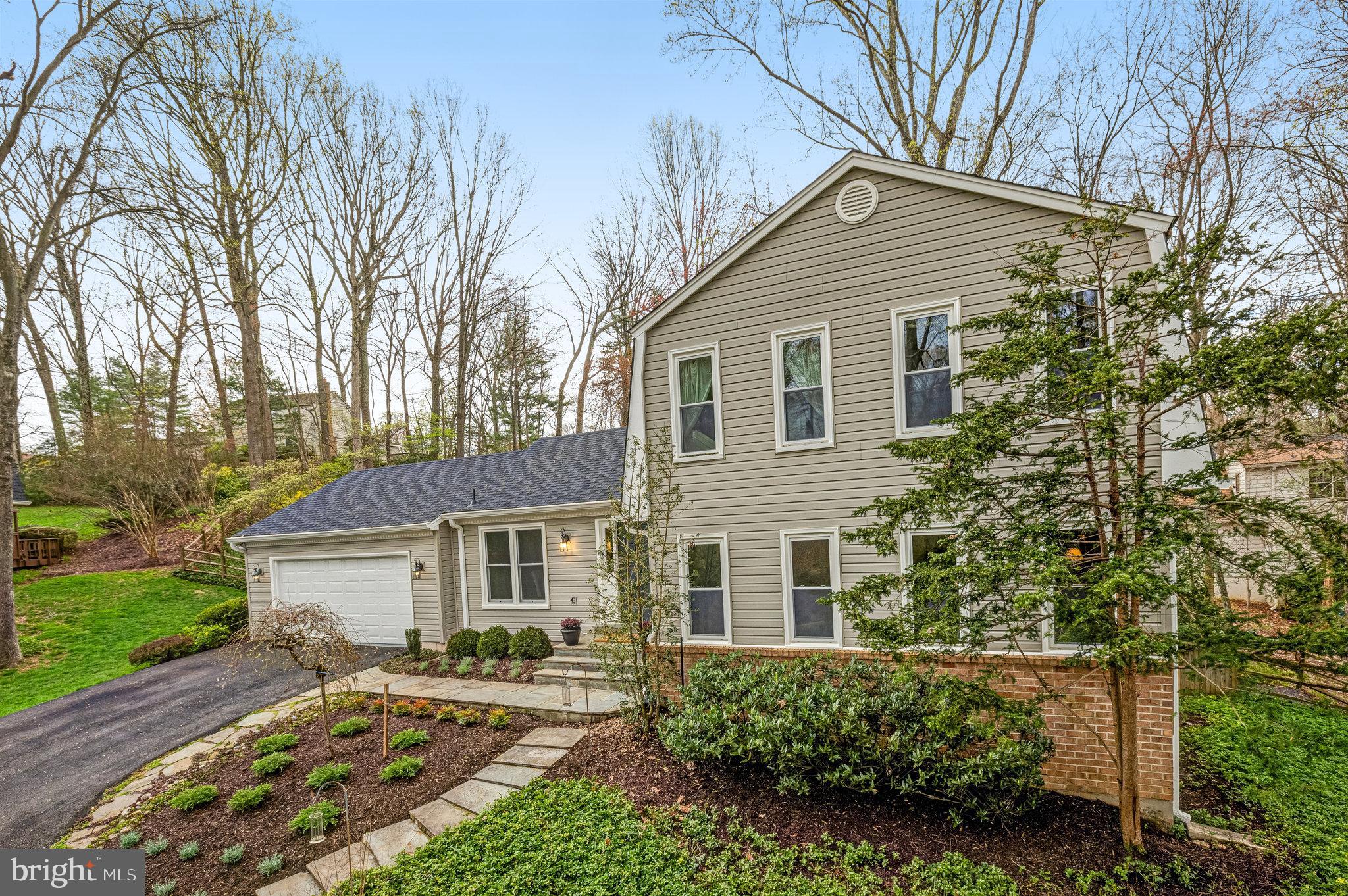 Two-story beige-sided house with an attached garage, brick foundation, and landscaped front yard.