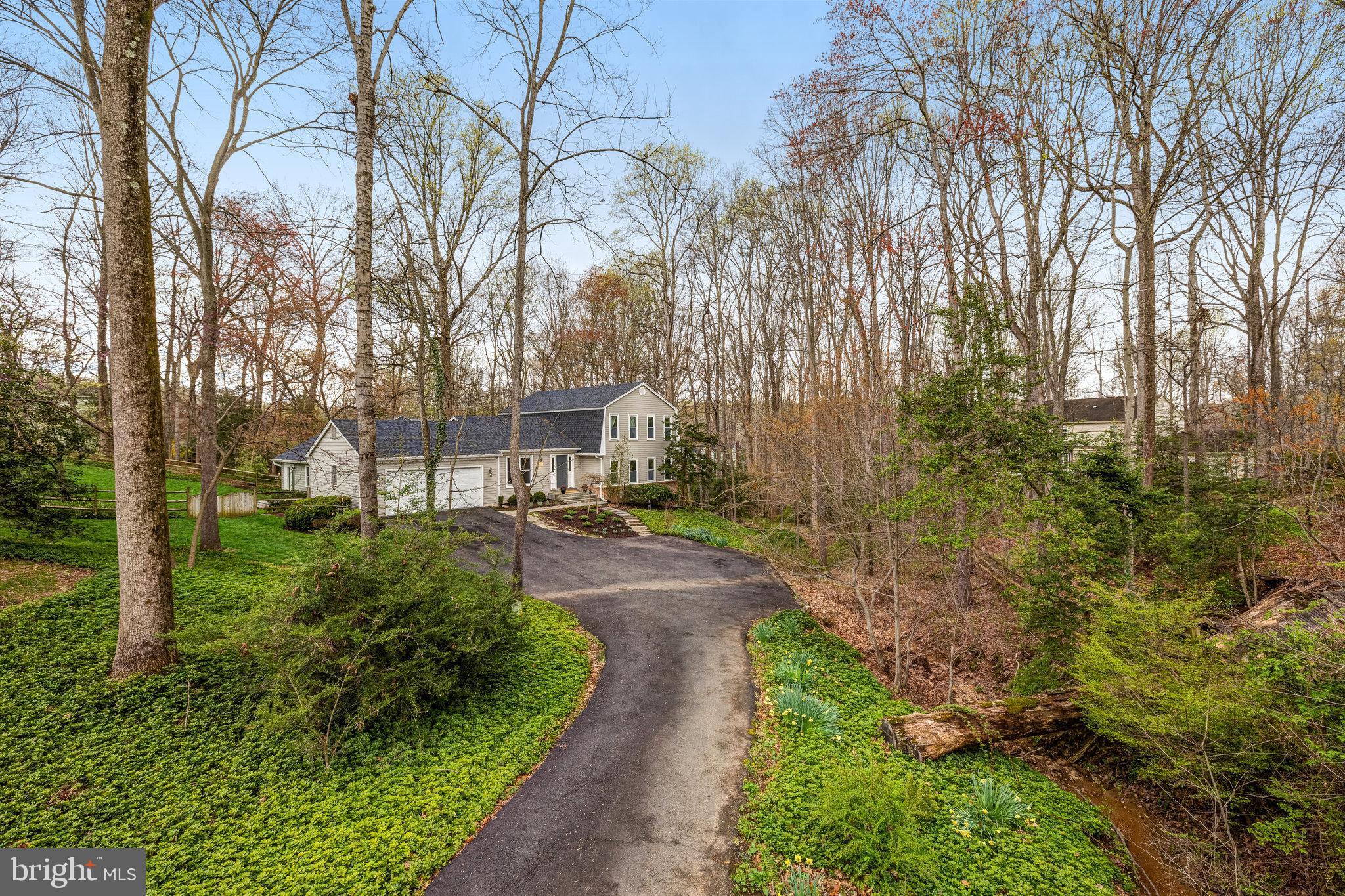Gray two-story house with an attached garage at the end of a curved driveway, surrounded by mature trees.