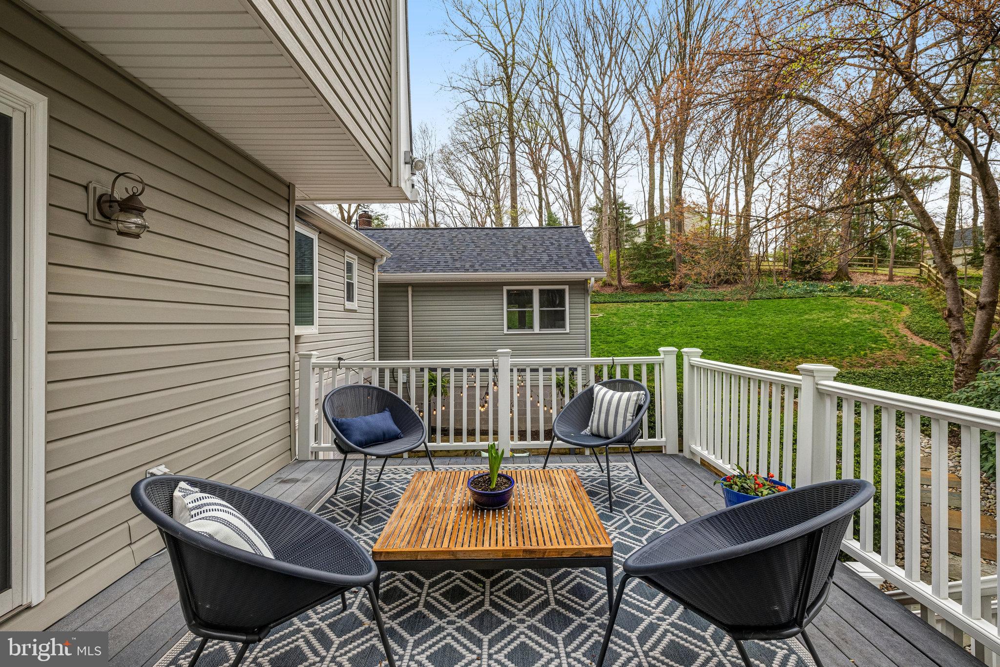 Furnished deck with black woven chairs and a wooden table overlooking a green lawn.