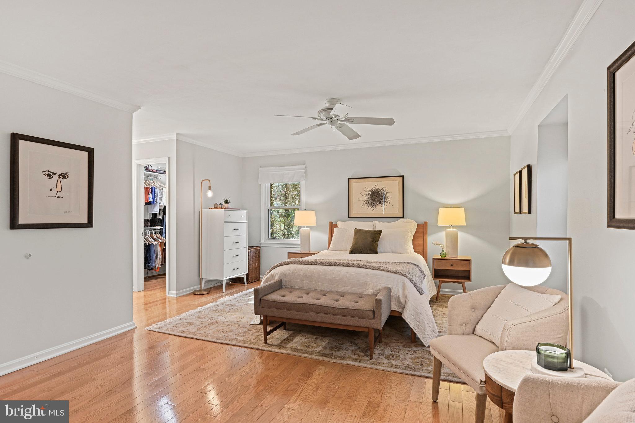 Staged bedroom with a wood bed, upholstered bench, hardwood floors, and an open walk-in closet.
