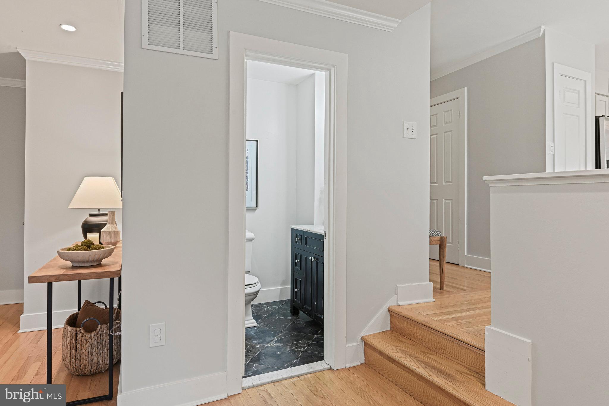 Hallway with hardwood floors and steps beside an open bathroom with a dark vanity.