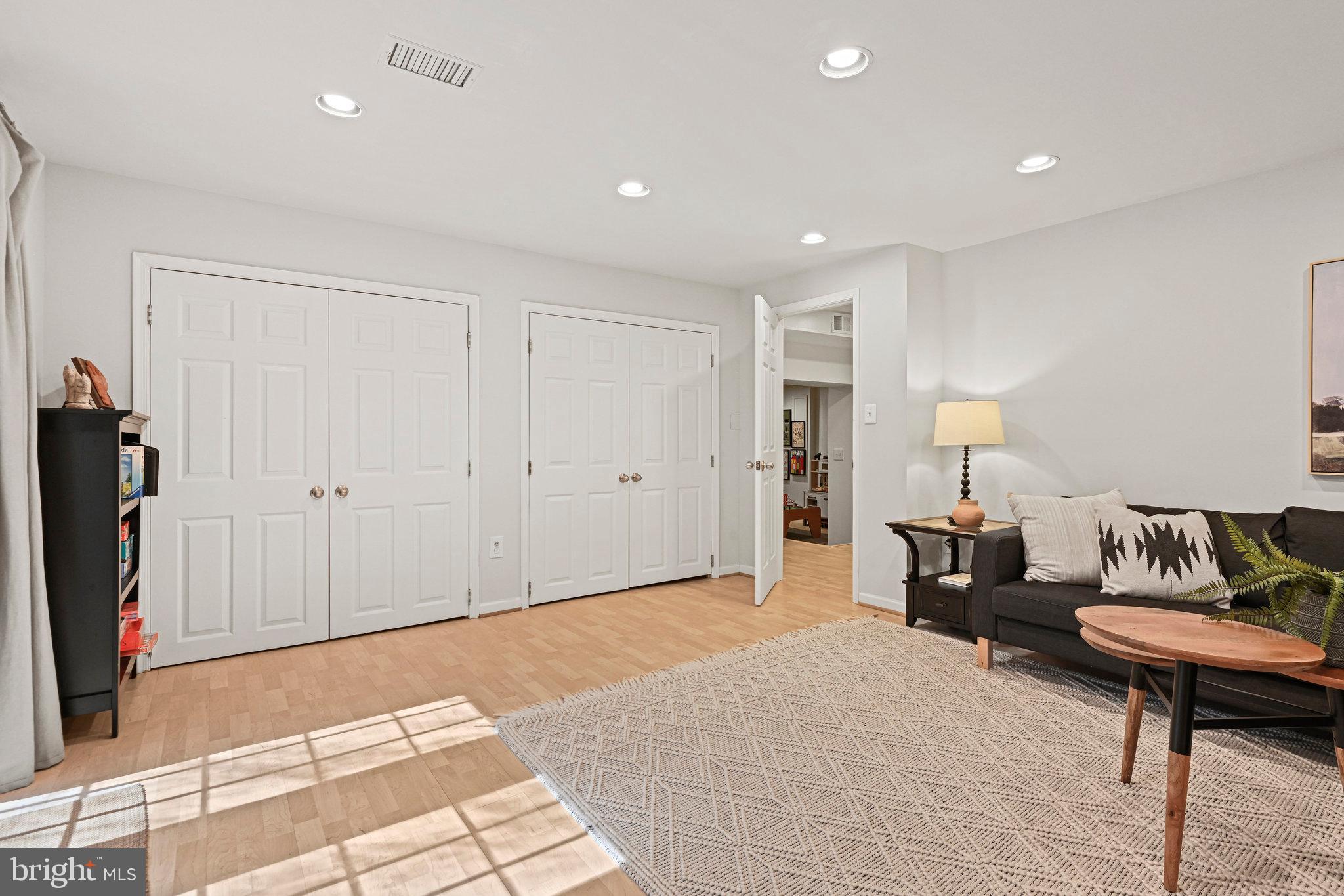 Living room with white closet doors, a dark sofa, and sunlight across the wood floor.
