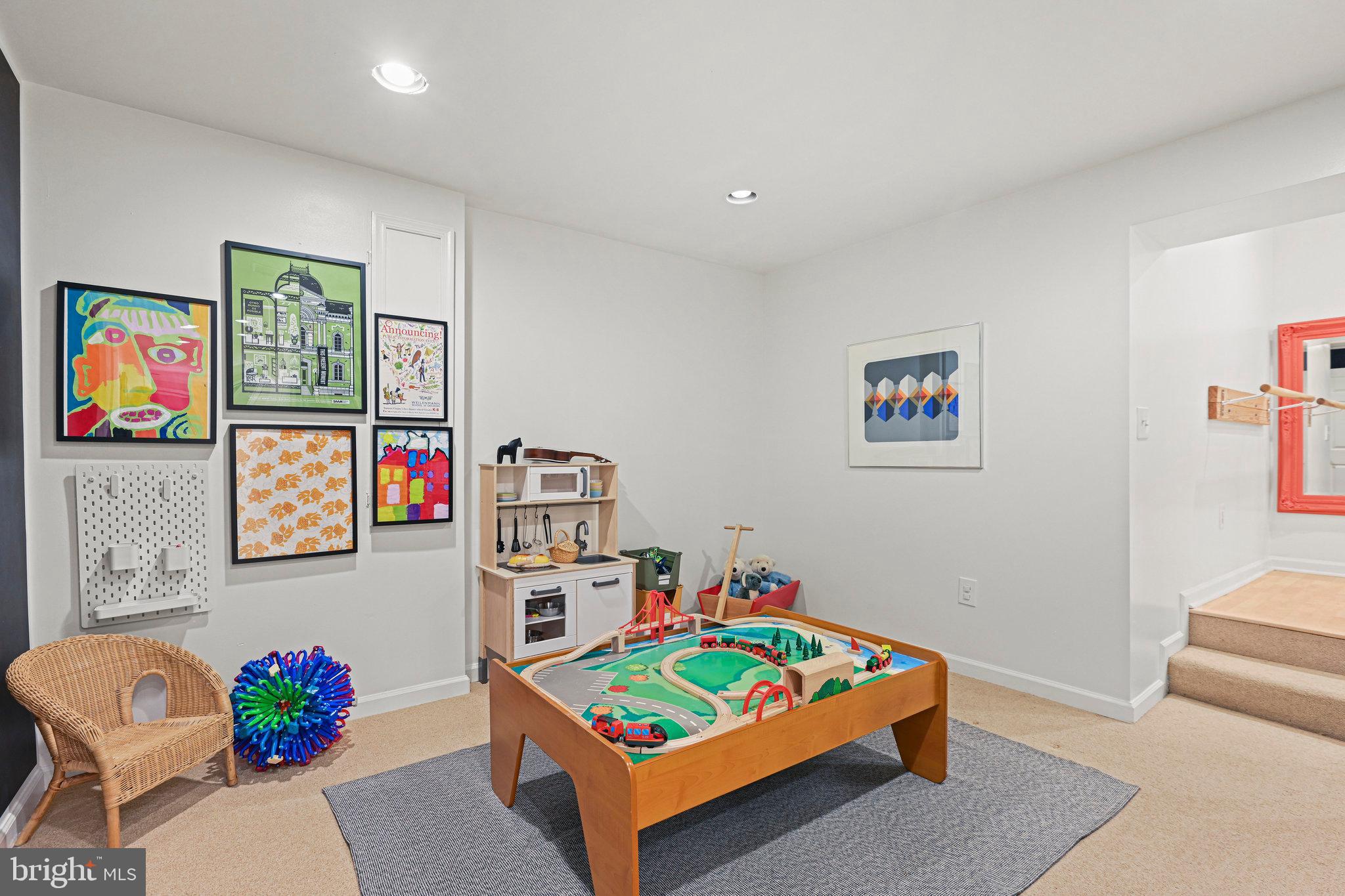 Children's playroom with a wooden train table, toy kitchen, colorful wall art, and steps to a raised area.
