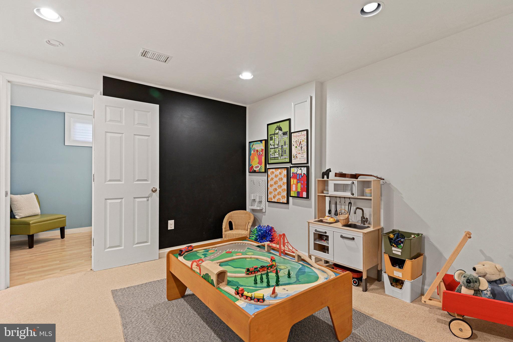 Children’s playroom with a wooden train table, toy kitchen, and colorful framed artwork.