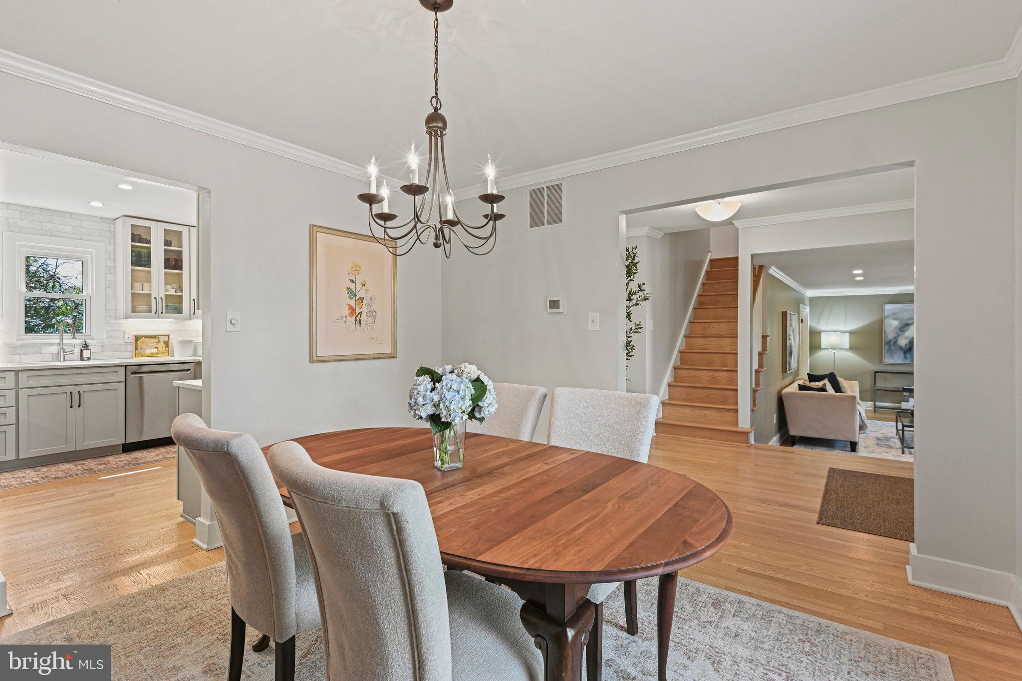 Dining room with an oval wood table and chandelier, opening to the kitchen and staircase.