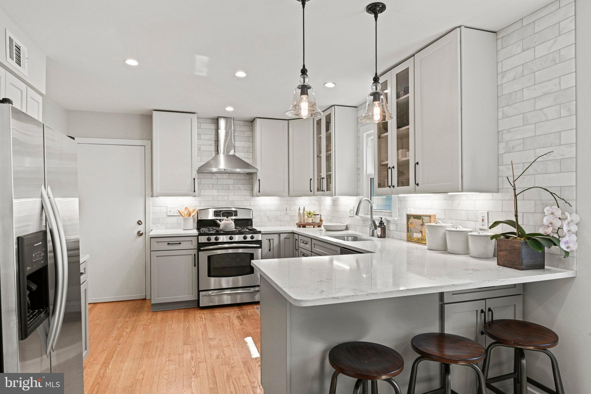 Kitchen with a large island, gray cabinets, stainless steel appliances, and three dark wood stools.