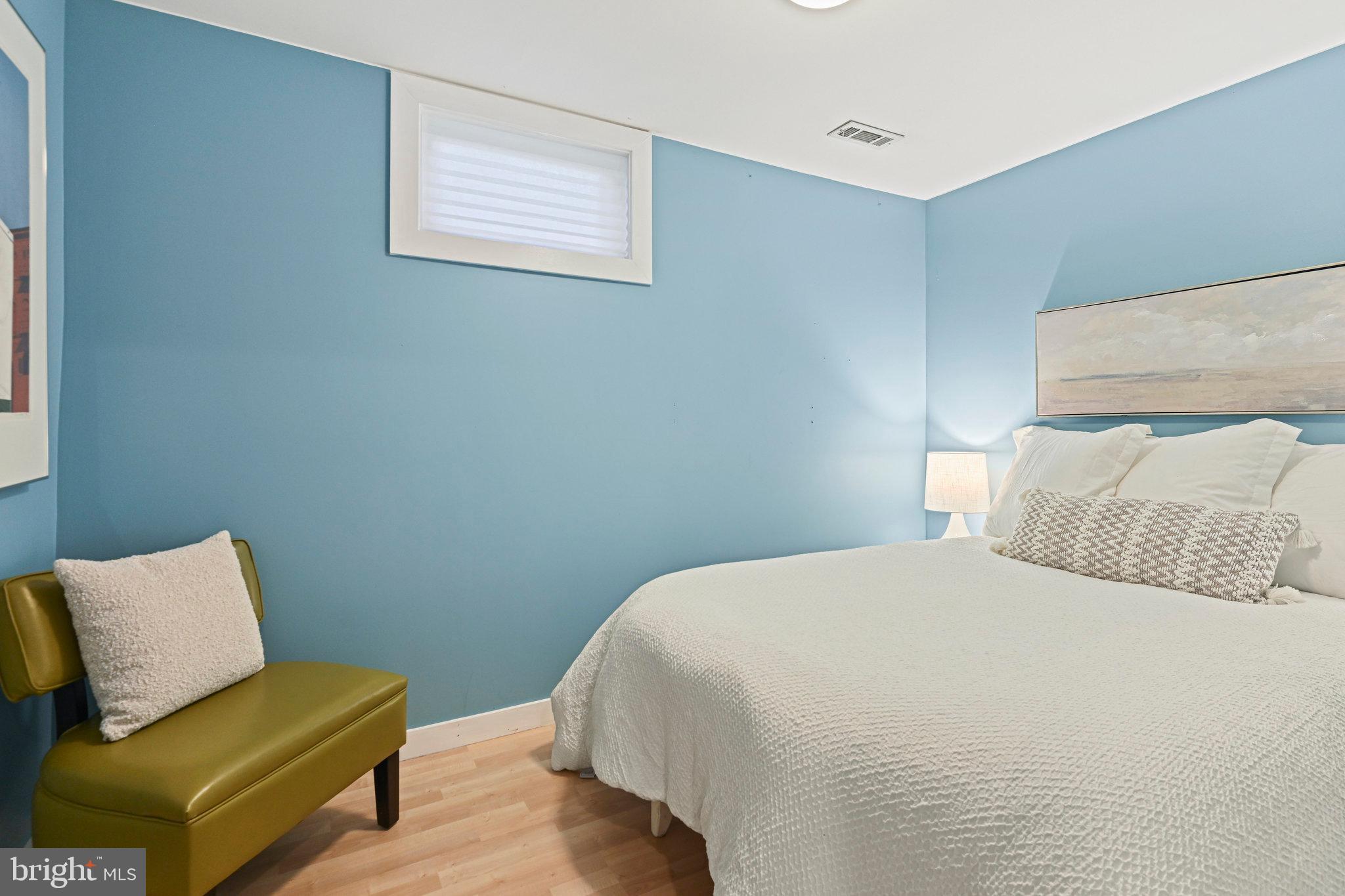 Bedroom with blue walls, a white bed, and an olive-green upholstered bench.