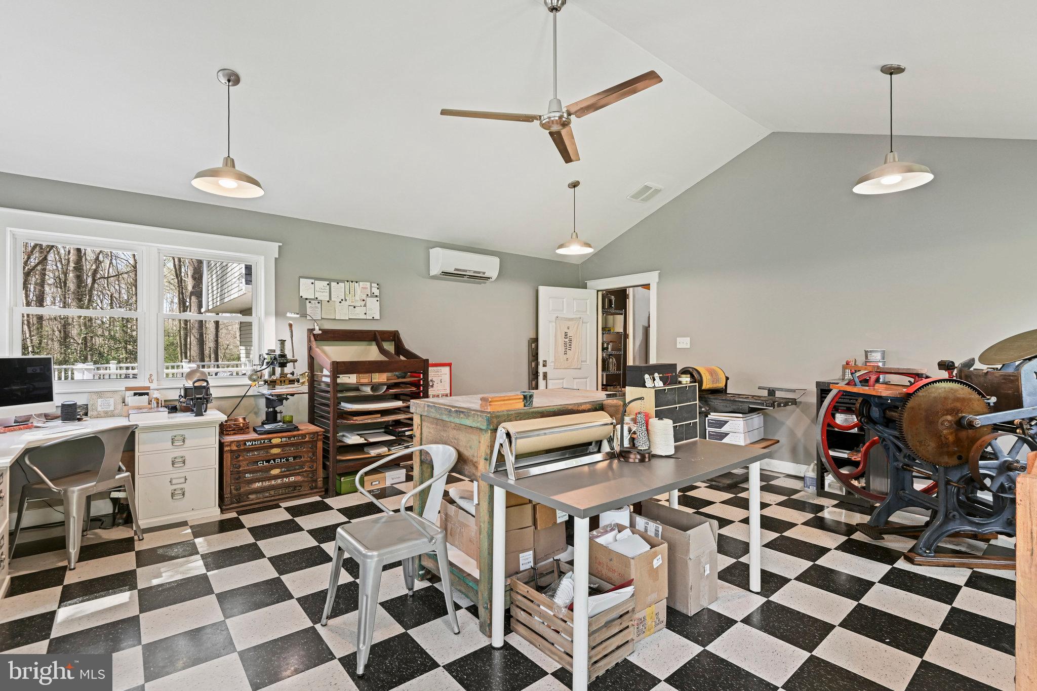 Workshop with printing equipment, worktables, large windows, and a checkerboard floor.
