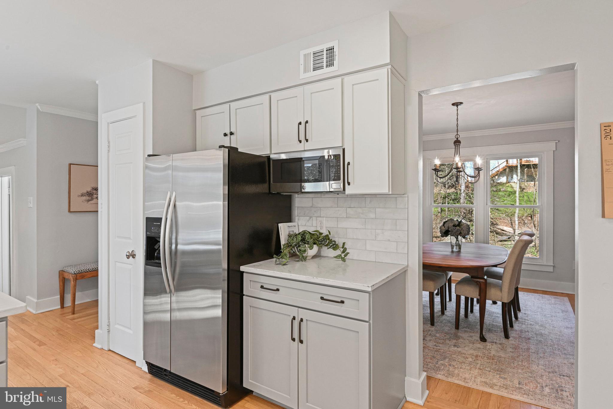 Kitchen with white cabinetry and stainless appliances, opening into a dining room with a wooden table and chandelier.