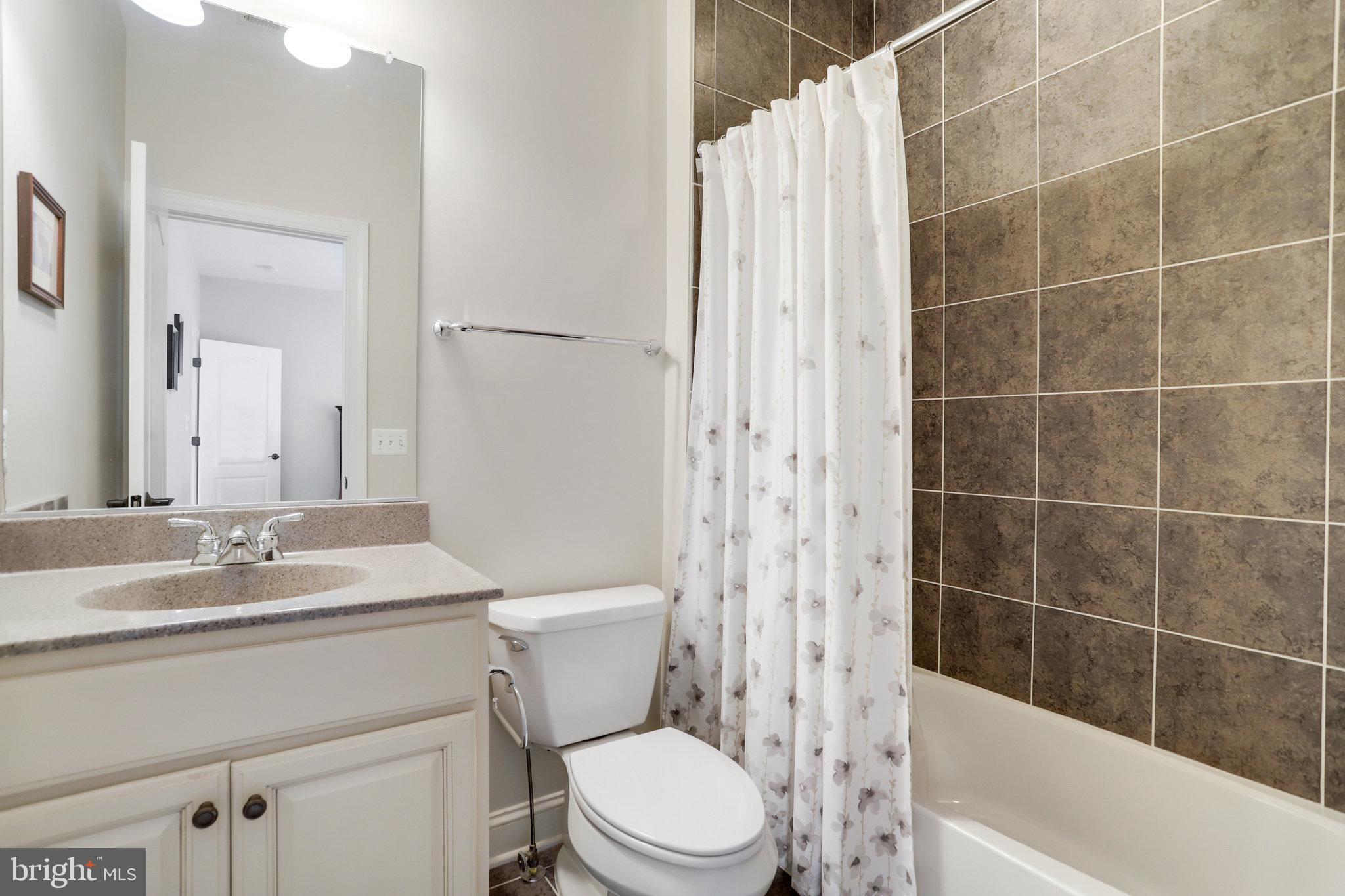 Bathroom with a white vanity, toilet, and tub bordered by large brown tiles.