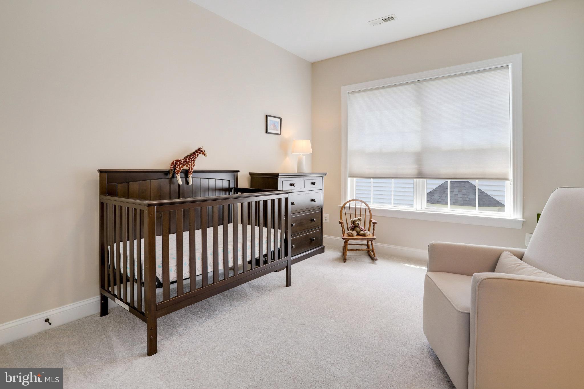 Furnished nursery with a dark wood crib, dresser, rocking chair, and large shaded window.