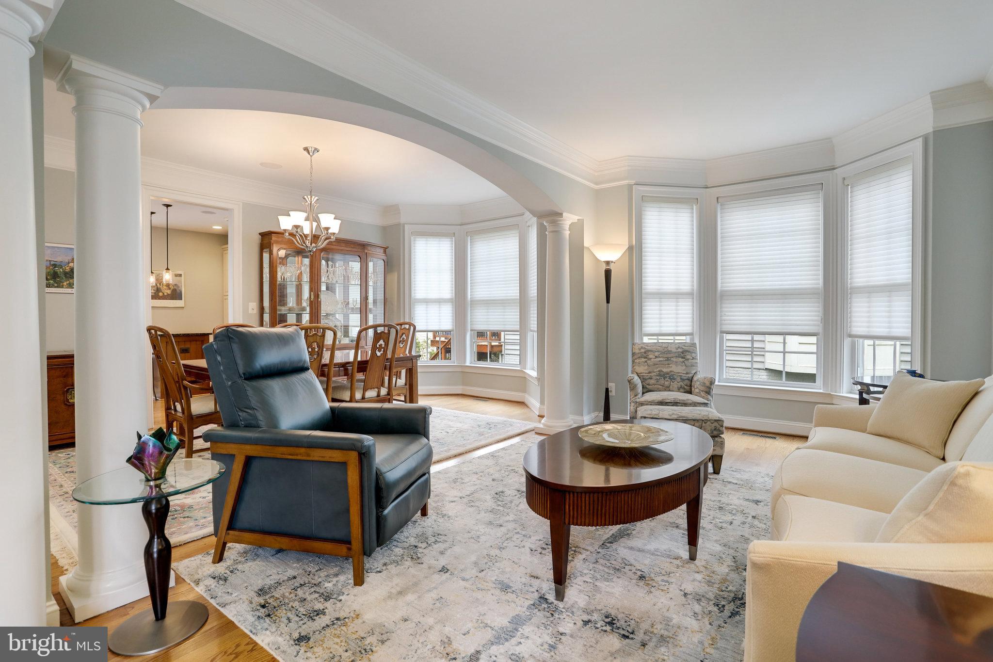 Living room with bay windows, white columns, a blue leather chair, and an adjoining dining area.