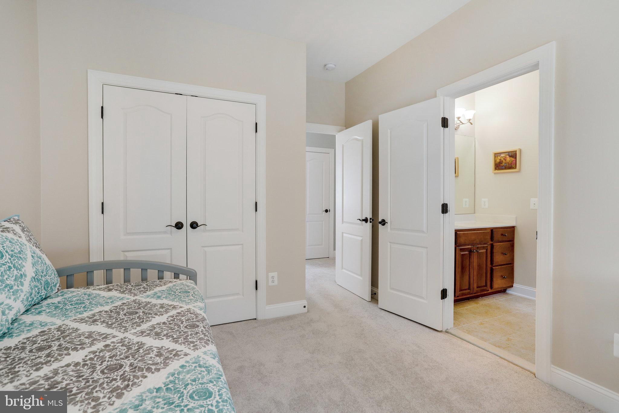 Bedroom with patterned bedding, white double closet doors, and an open bathroom doorway.
