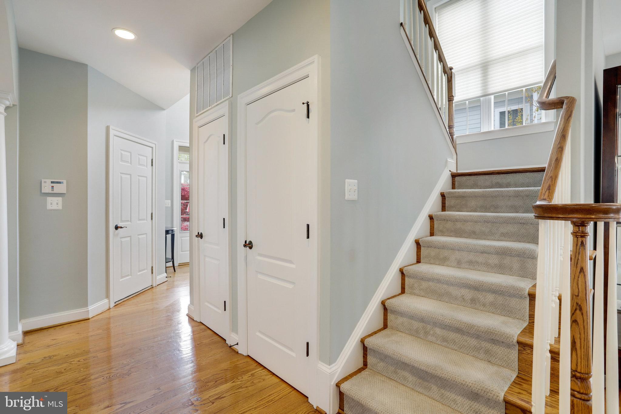 Entry hall with carpeted staircase, wood handrail, hardwood floors, and a tall window.
