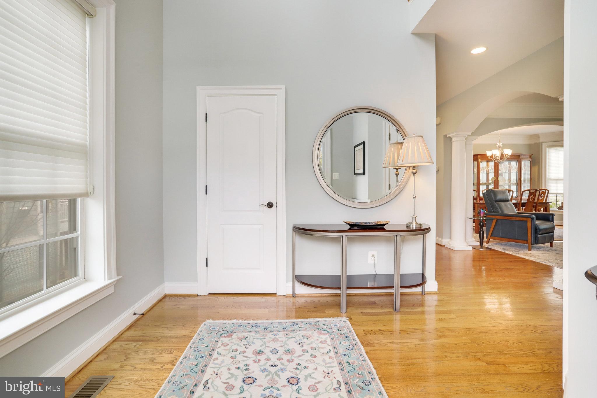 Furnished entryway with hardwood floors, a round mirror, and an arched opening to the living and dining areas.