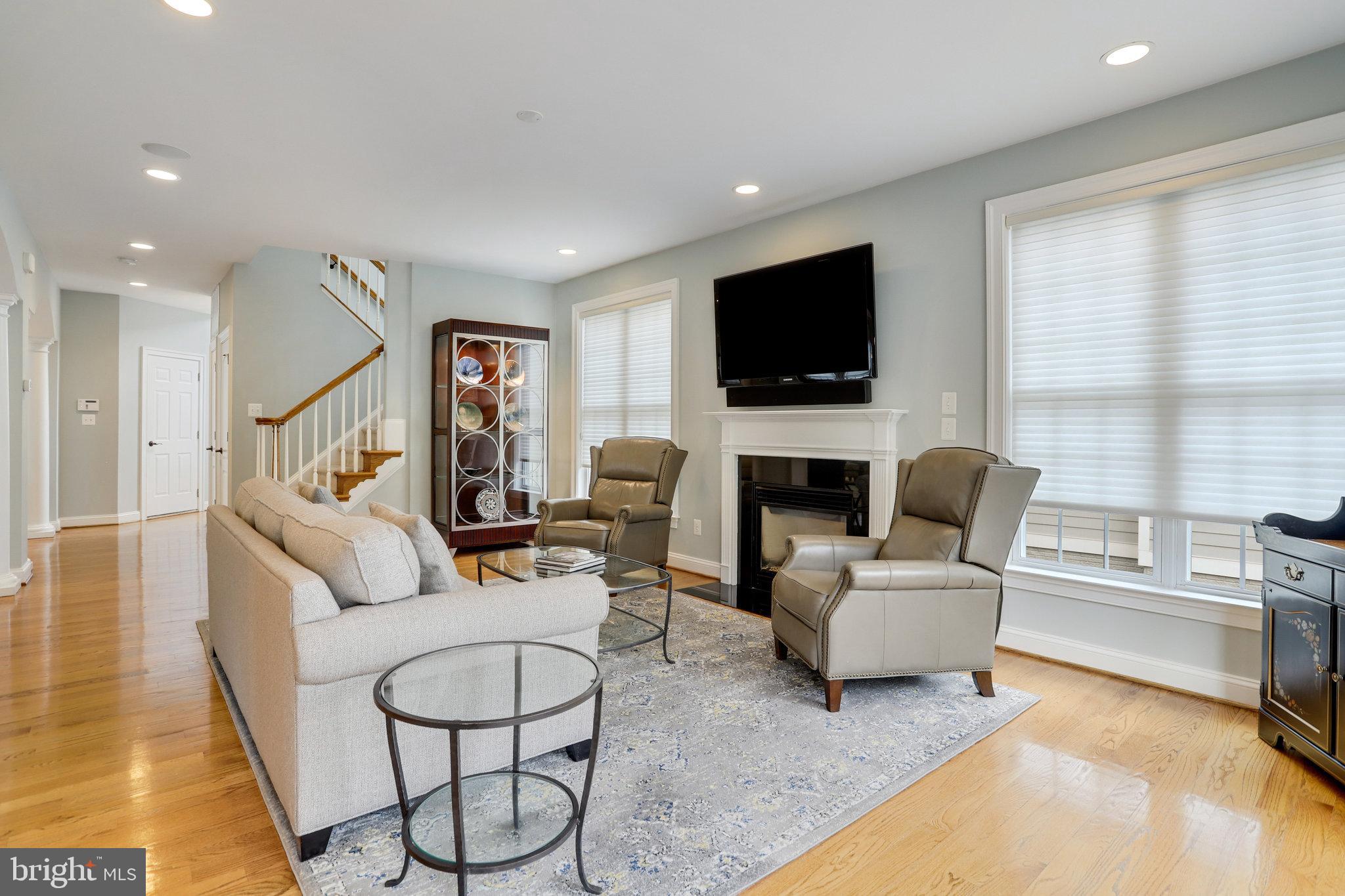 Living room with a fireplace, wall-mounted TV, hardwood floors, and staircase.