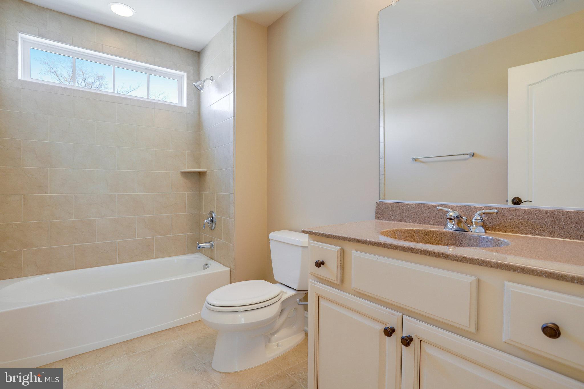 Bathroom with a tiled bathtub, high horizontal window, and long vanity beneath a large mirror.