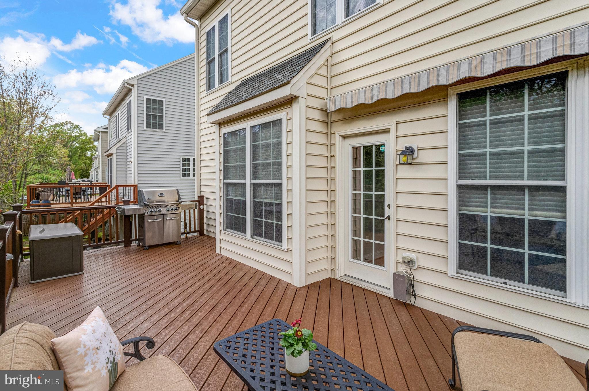 Furnished composite deck with patio seating, a grill, and hot tub beside a beige-sided home.