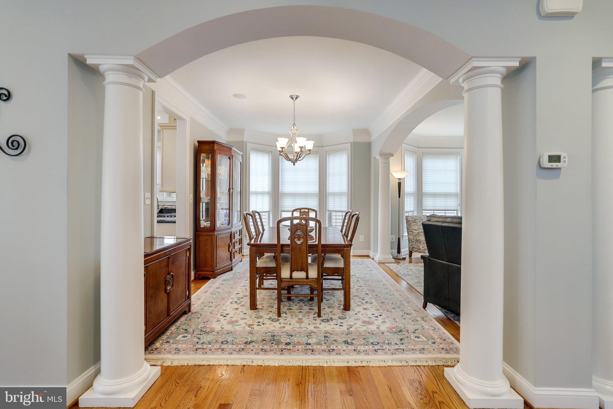 Dining room with a wooden table, chandelier, patterned rug, and arched entry with white columns.