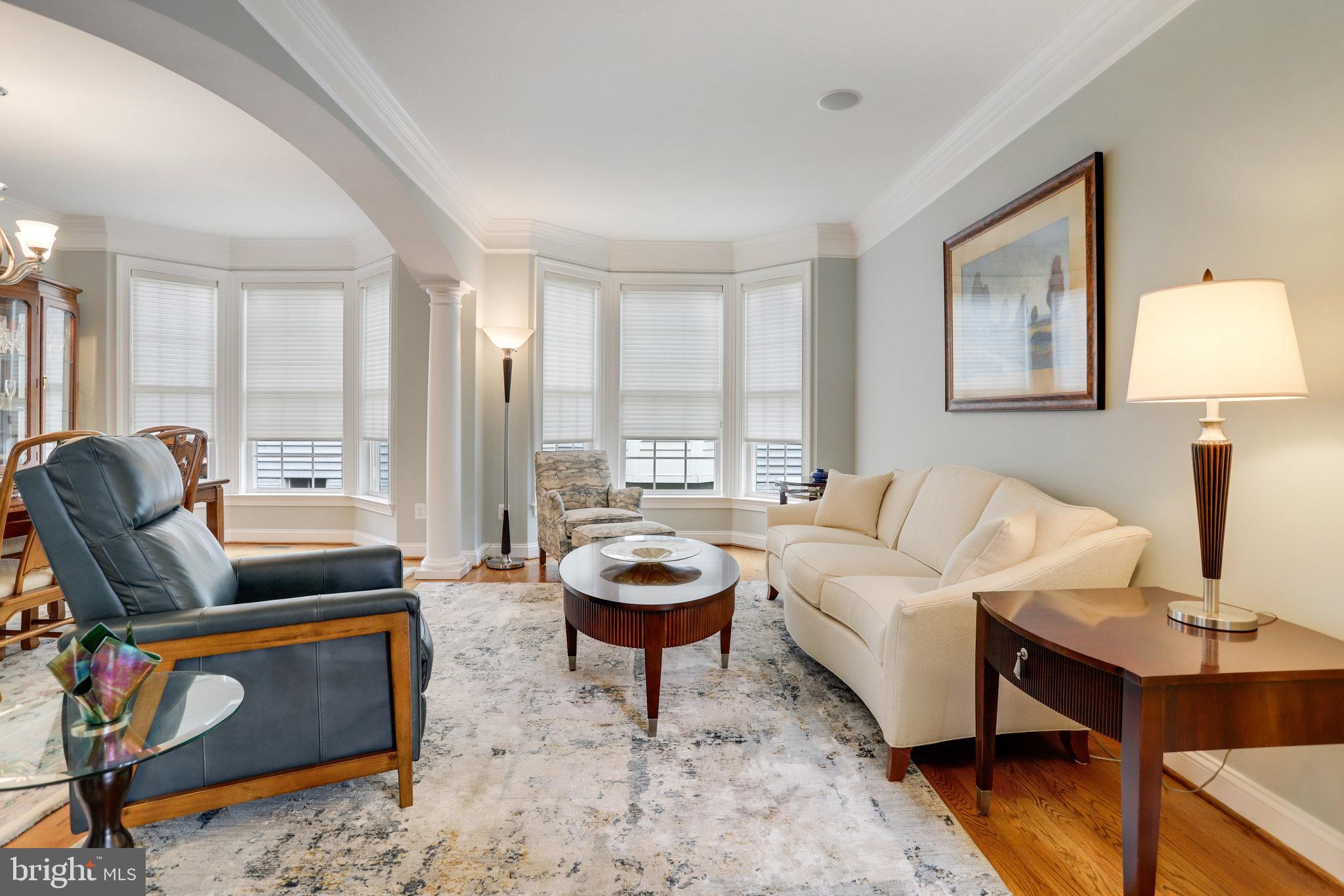 Living room with bay windows, a cream sofa, dark leather armchair, and round coffee table.
