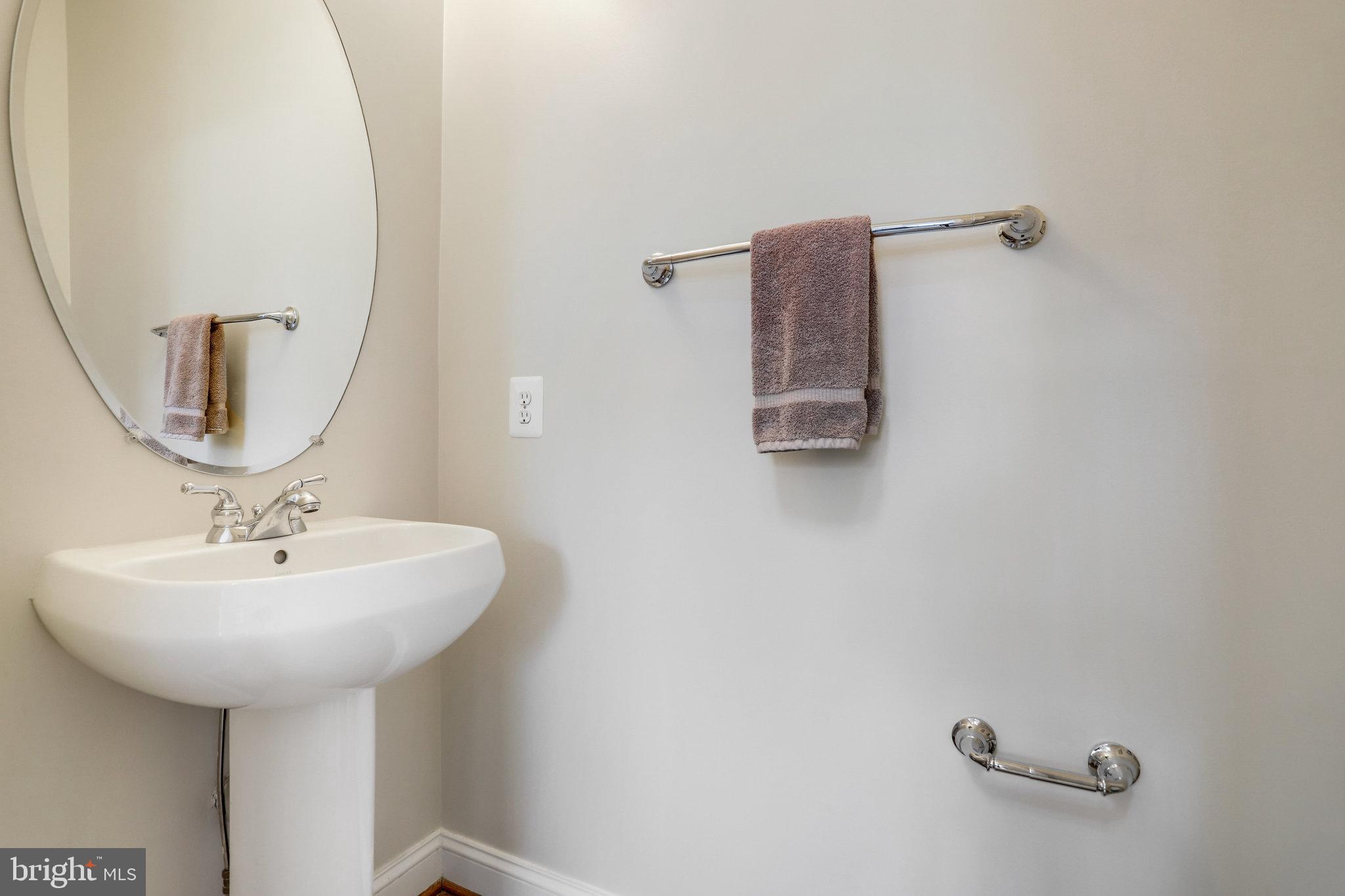 Bathroom with a pedestal sink, oval mirror, mauve towel, and chrome grab bars.
