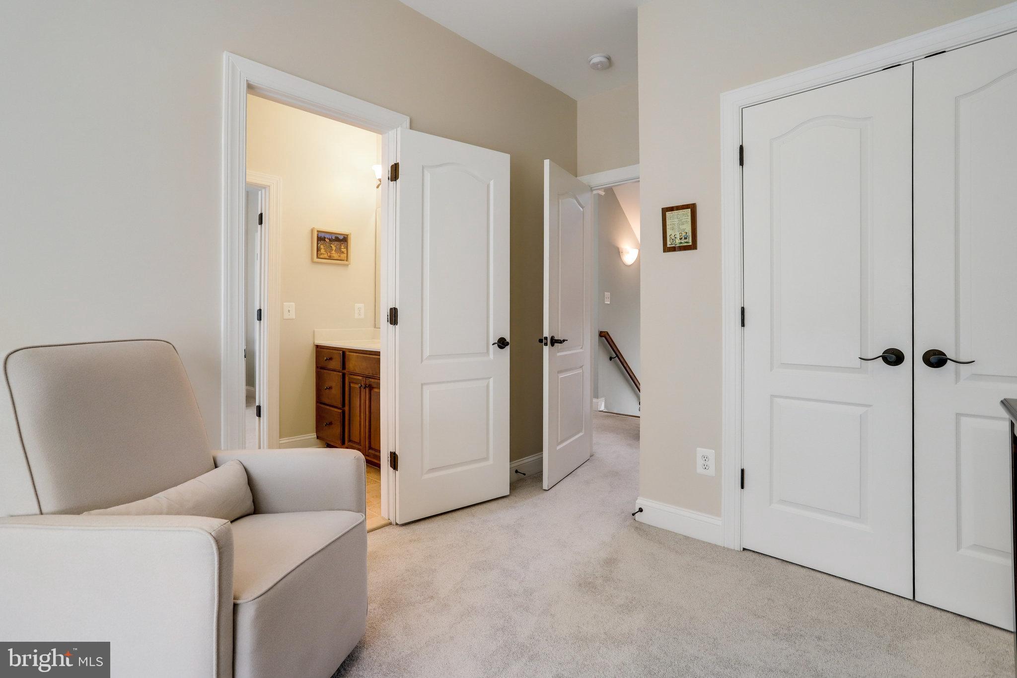 Carpeted bedroom with a light armchair, double closet doors, and open doorways to a bathroom and stair landing.