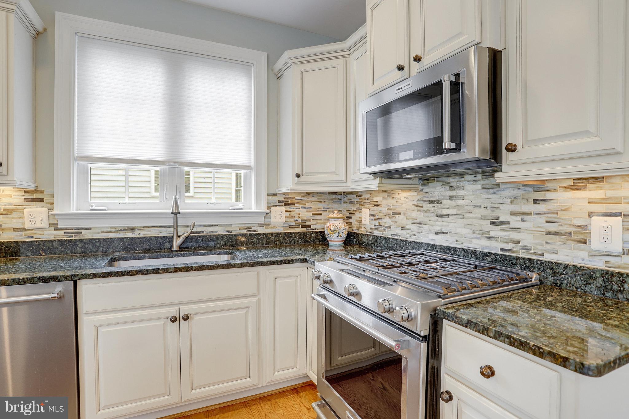 Kitchen with cream cabinets, granite counters, mosaic backsplash, and stainless steel range and microwave.