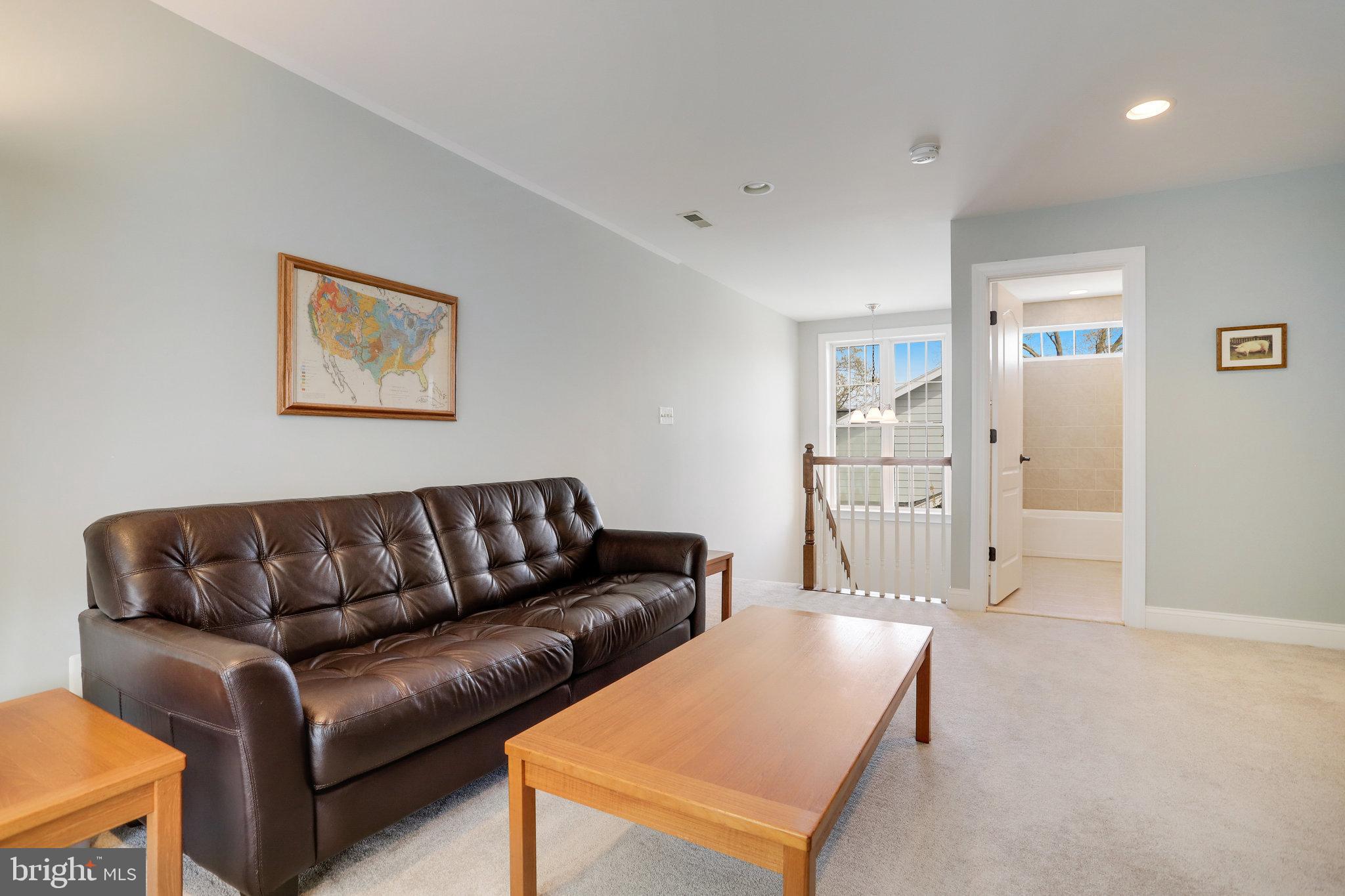 Living room with a dark leather sofa, wooden coffee table, and window beside an open bathroom doorway.